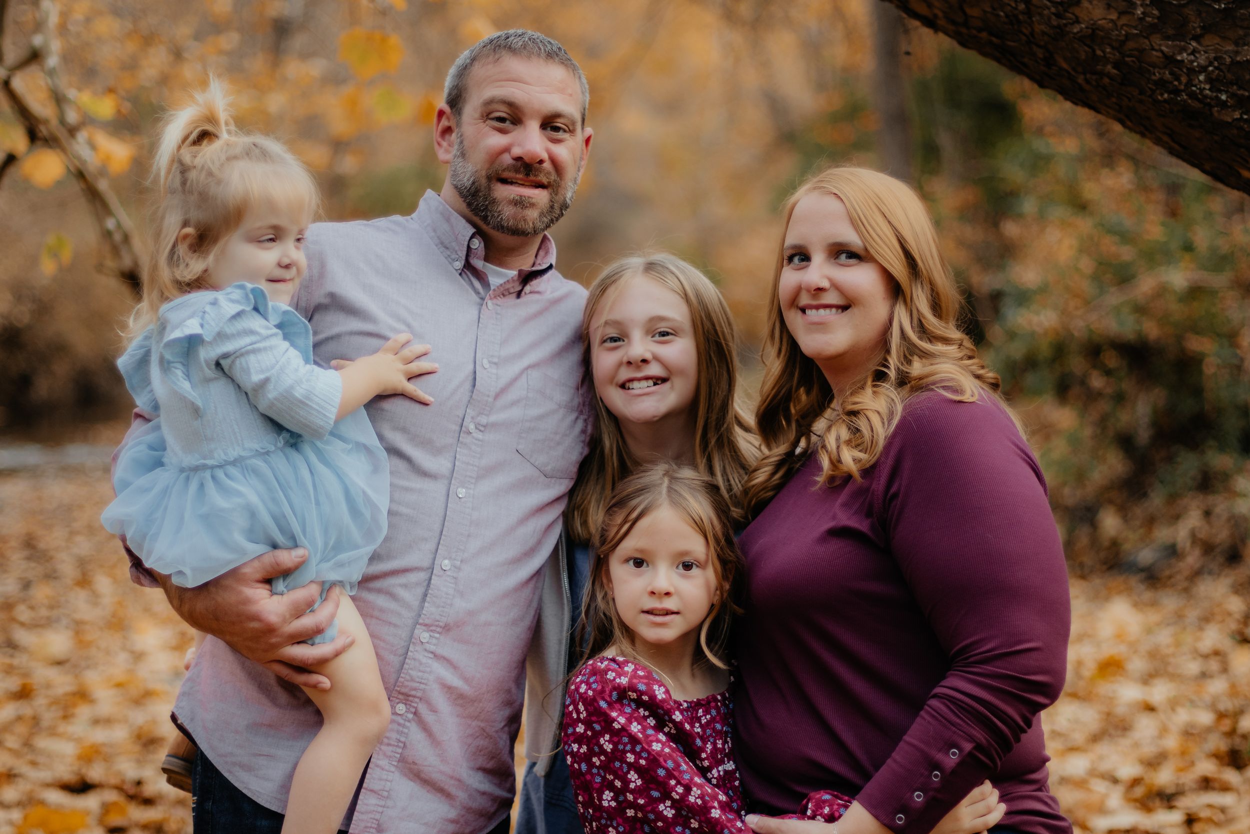 A warm family portrait captured outdoors during autumn with golden leaves in the background.