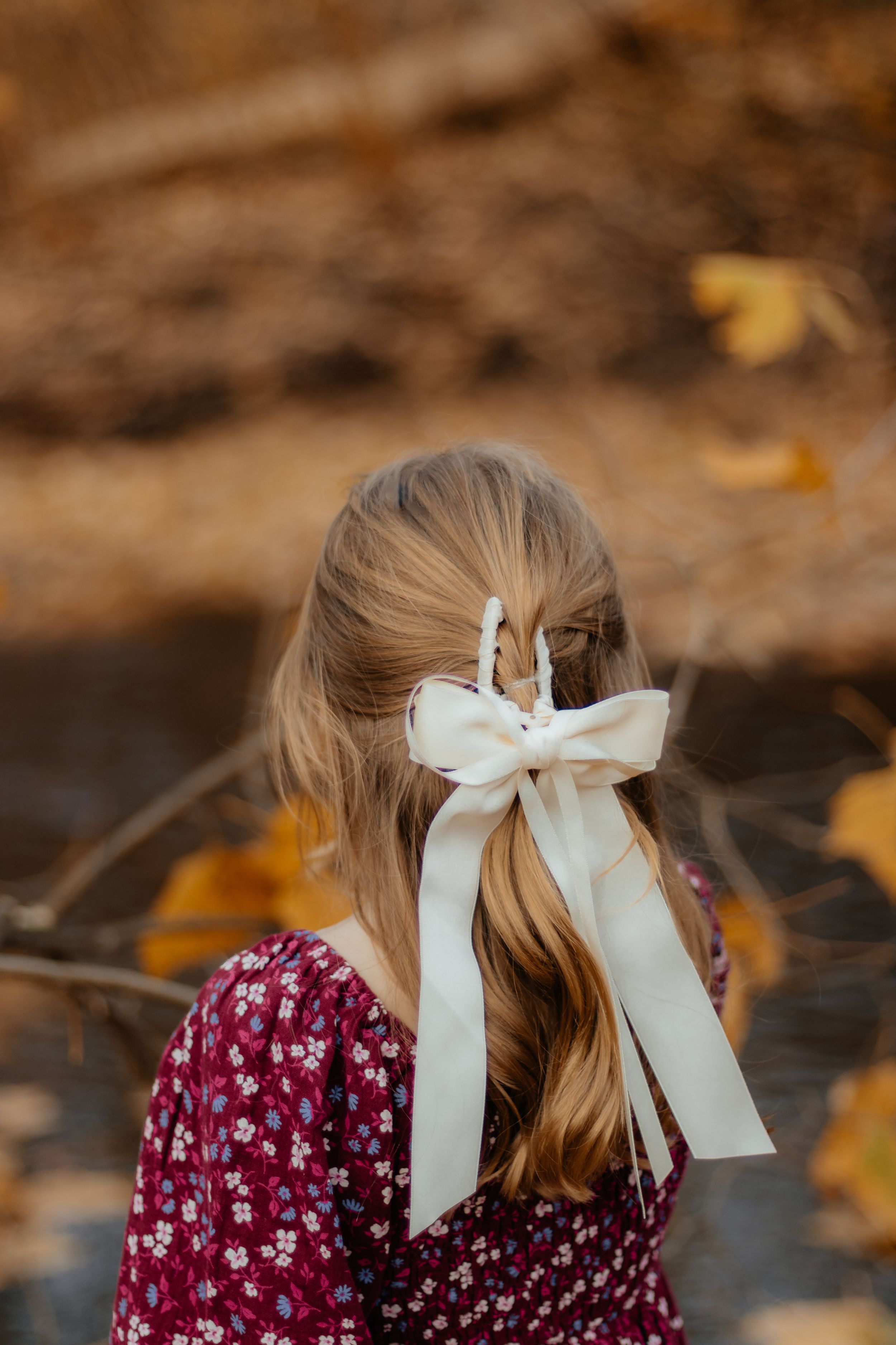 Close up view of white hair ribbons tied in bows against burgundy floral dress.