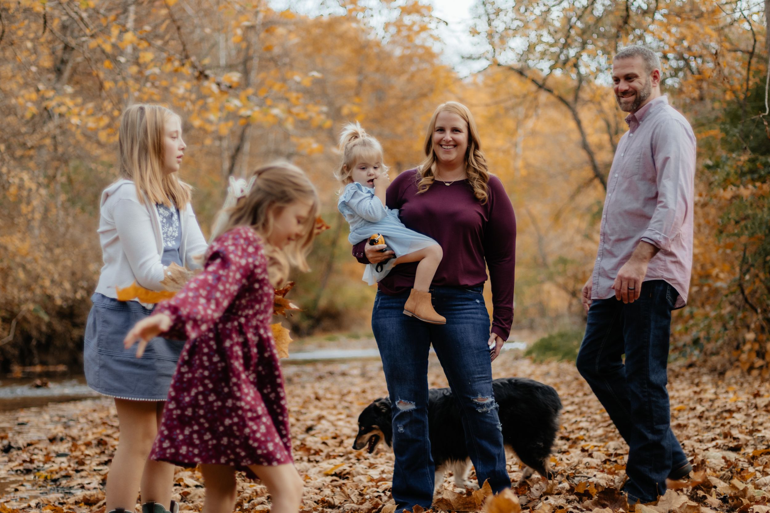 A family plays together in fallen autumn leaves during an outdoor photo session.