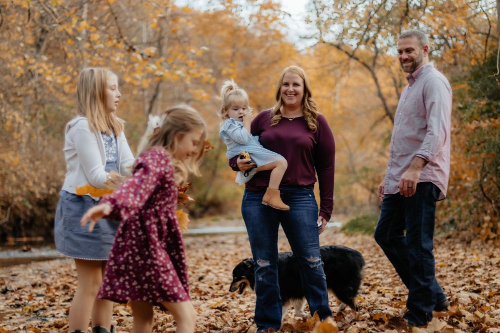 A family plays together in fallen autumn leaves during an outdoor photo session.