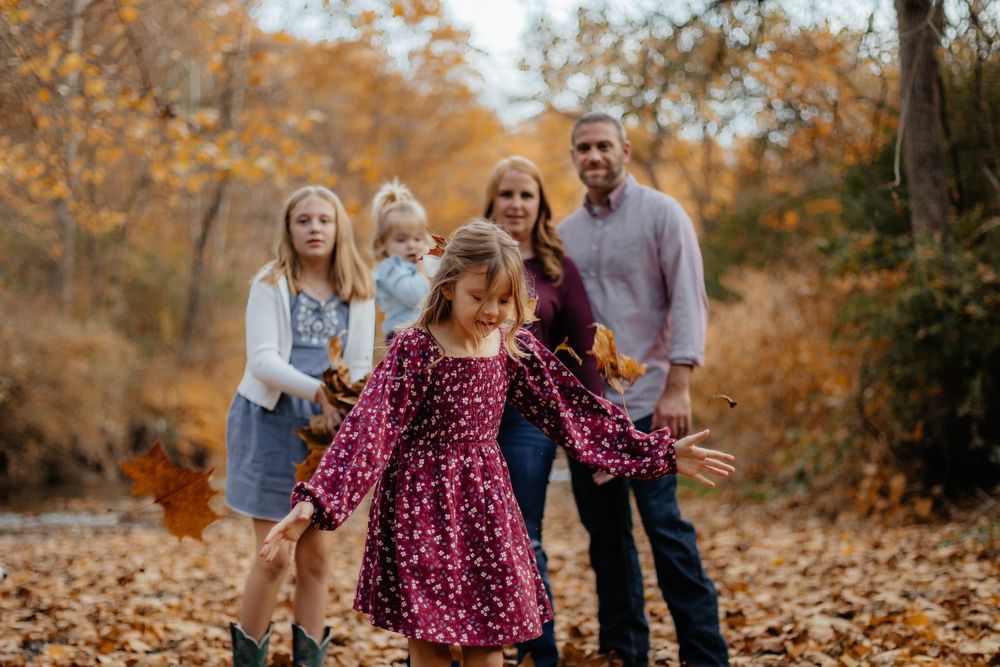 Family members throw autumn leaves in the air during a playful outdoor photoshoot.