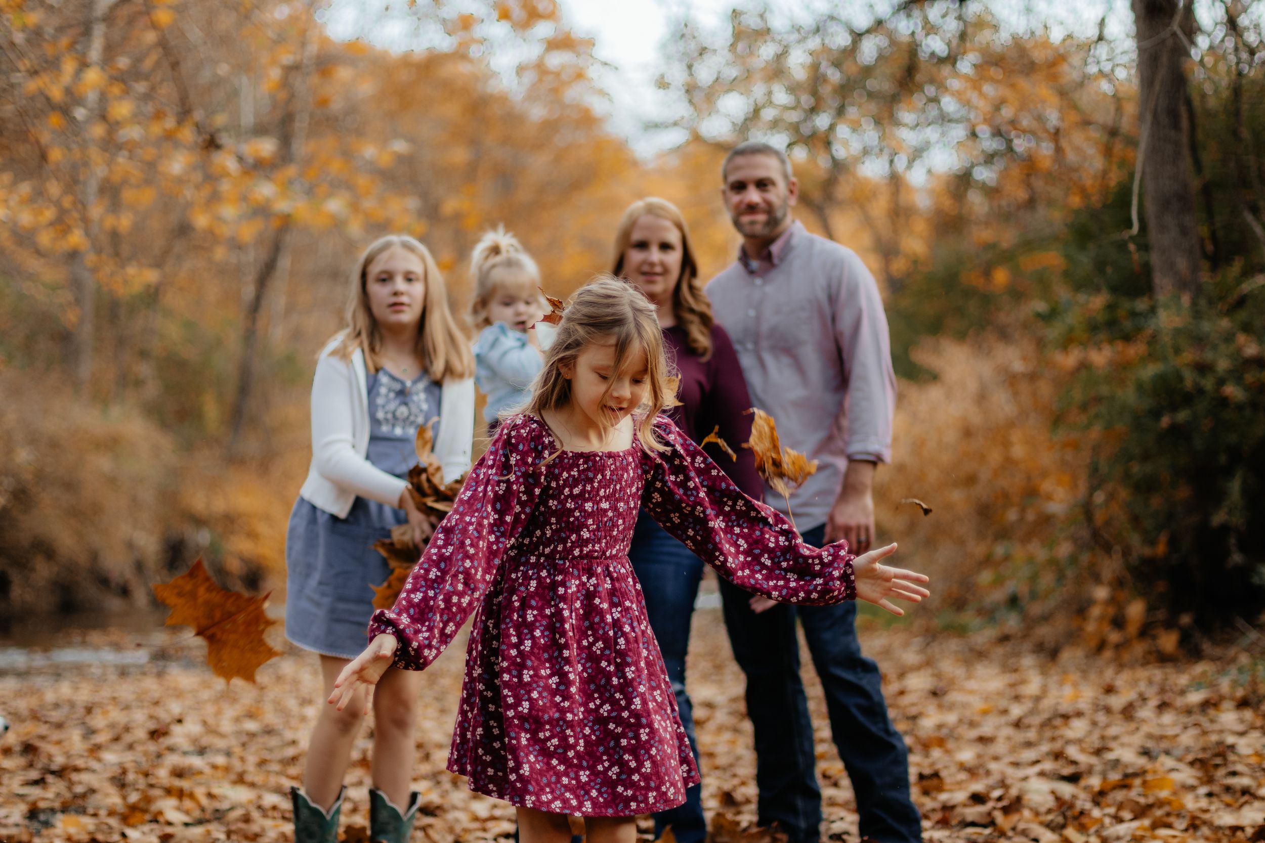 Family members throw autumn leaves in the air during a playful outdoor photoshoot.