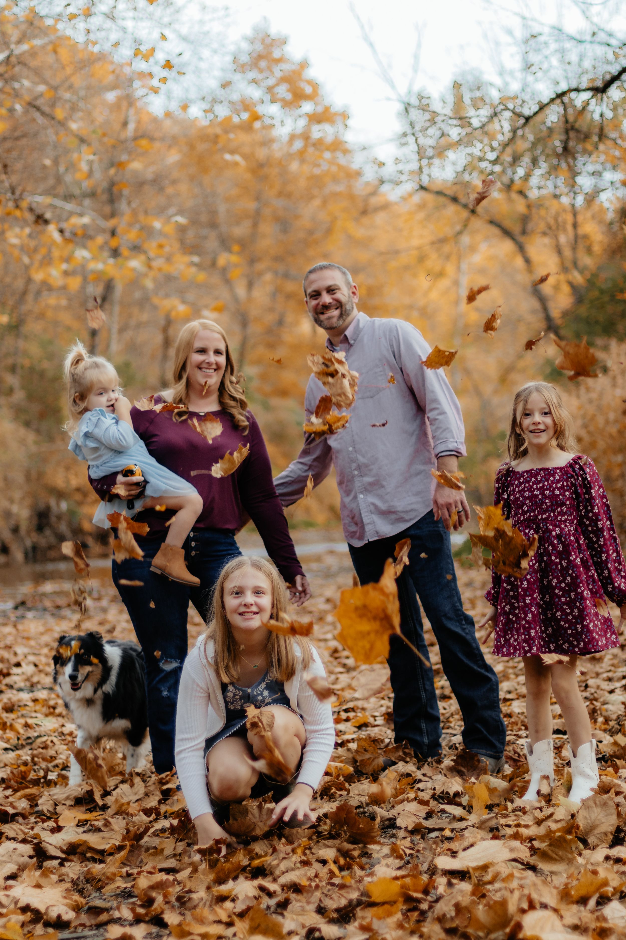 Family members throw leaves and play together during a fall photo session.