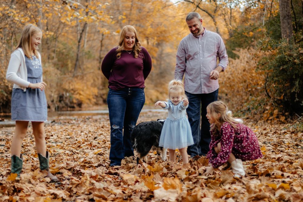 Family enjoying a fall photoshoot together in a forest covered with golden autumn leaves.