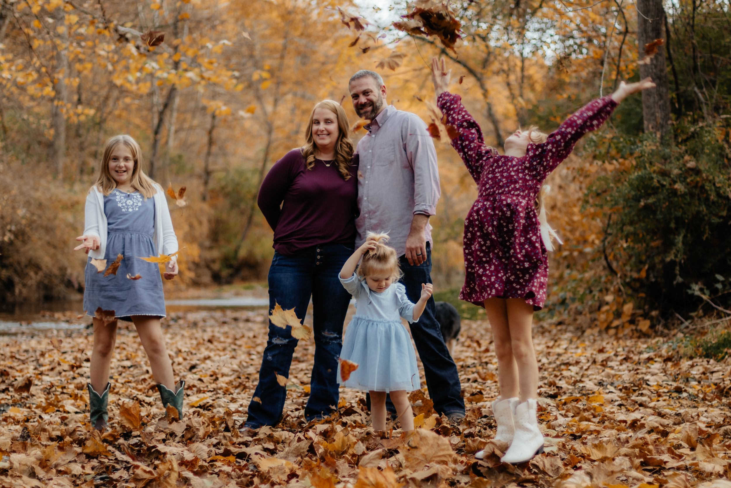 Family having fun and playing in fallen autumn leaves during an outdoor photo session.