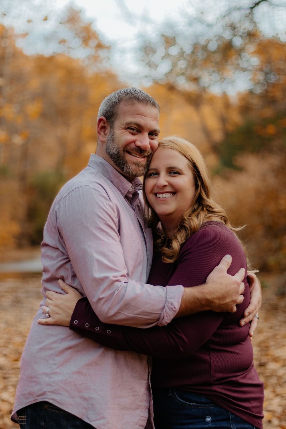 Couple embracing and laughing together during autumn photo session with golden foliage in background.