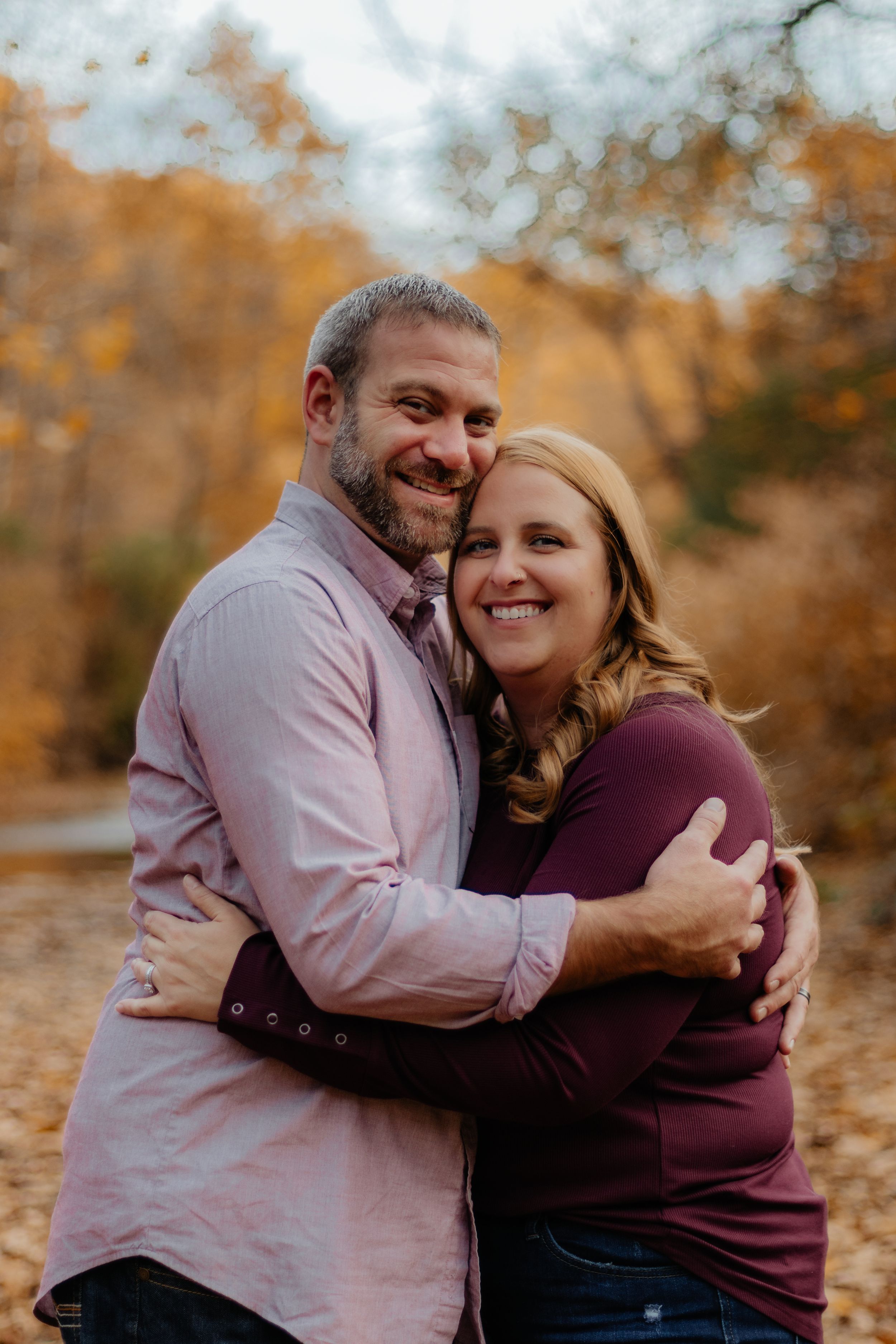 Couple embracing and laughing together during autumn photo session with golden foliage in background.