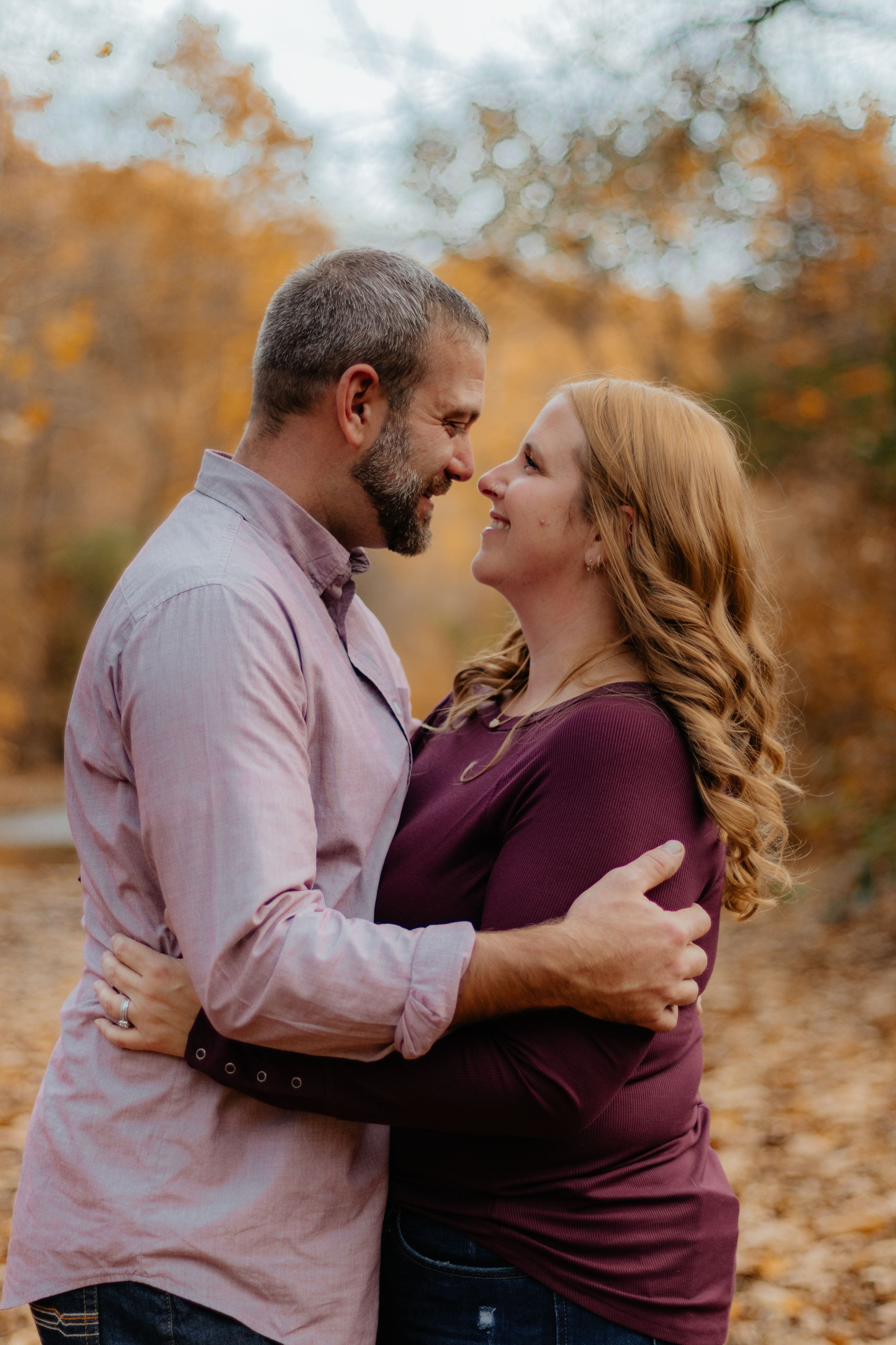 Romantic couple sharing intimate moments during fall photoshoot surrounded by autumn leaves.