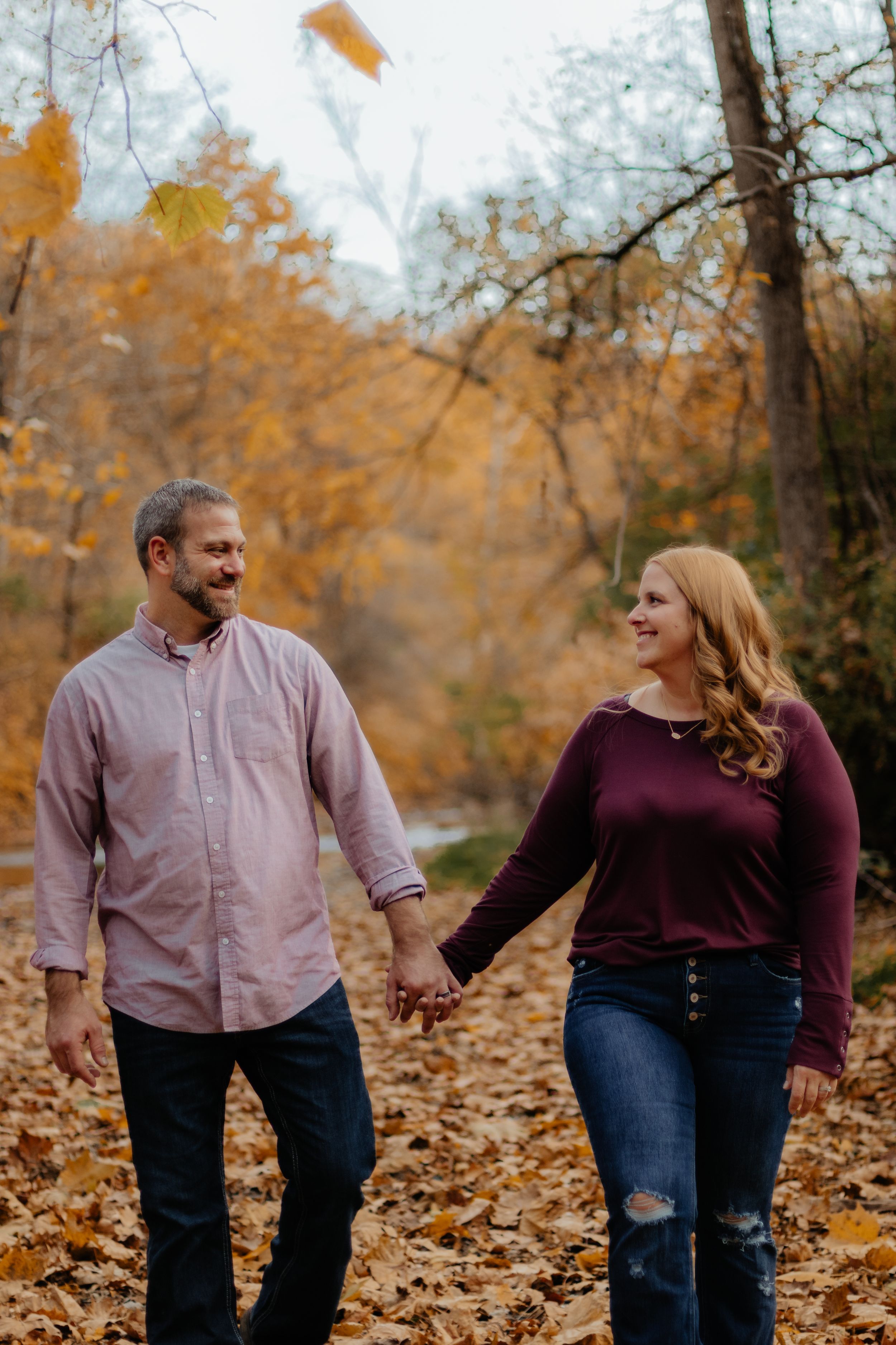 Couple strolling together through autumn forest while holding hands and smiling.