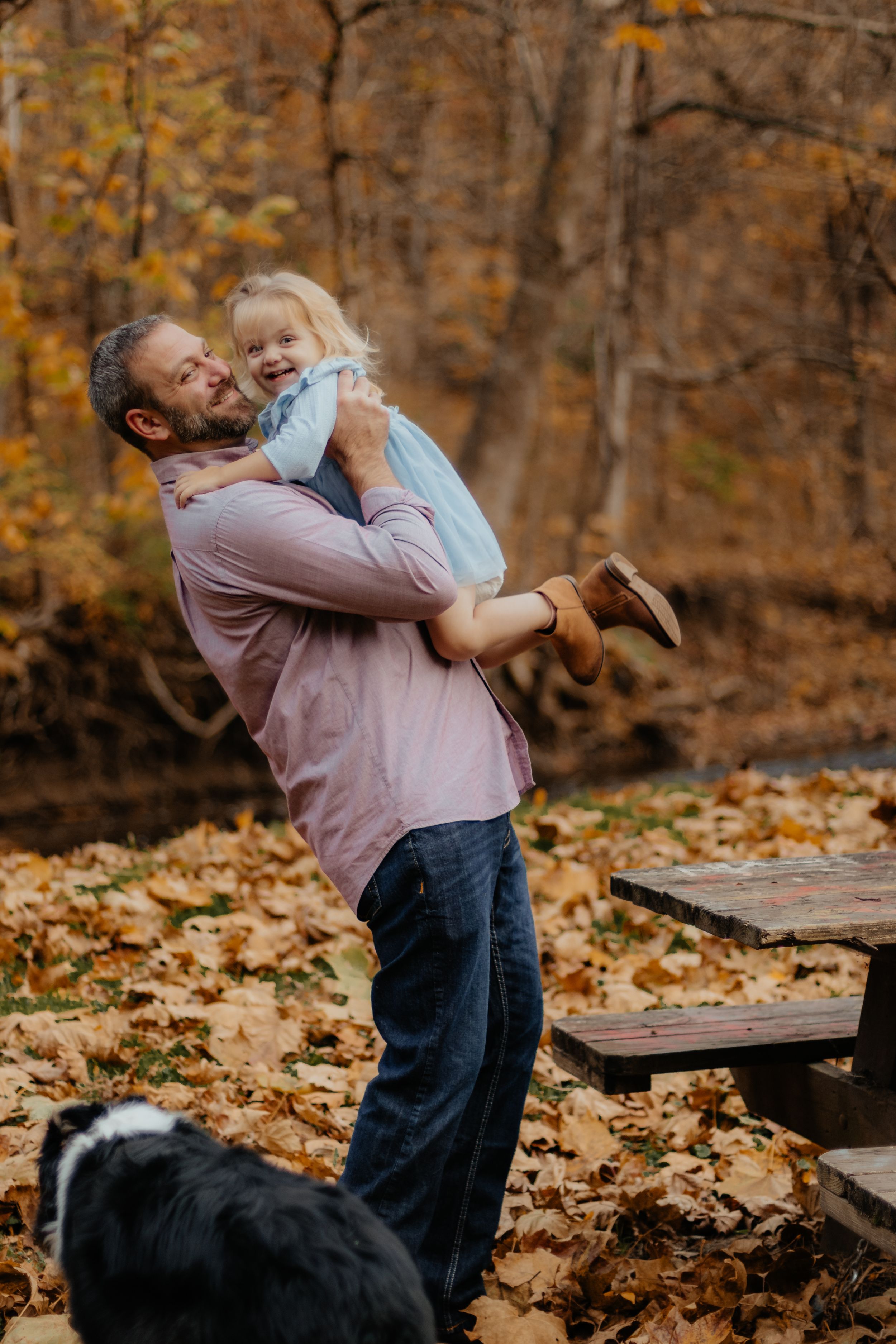 Joyful outdoor autumn photoshoot with family and dog among fallen leaves.