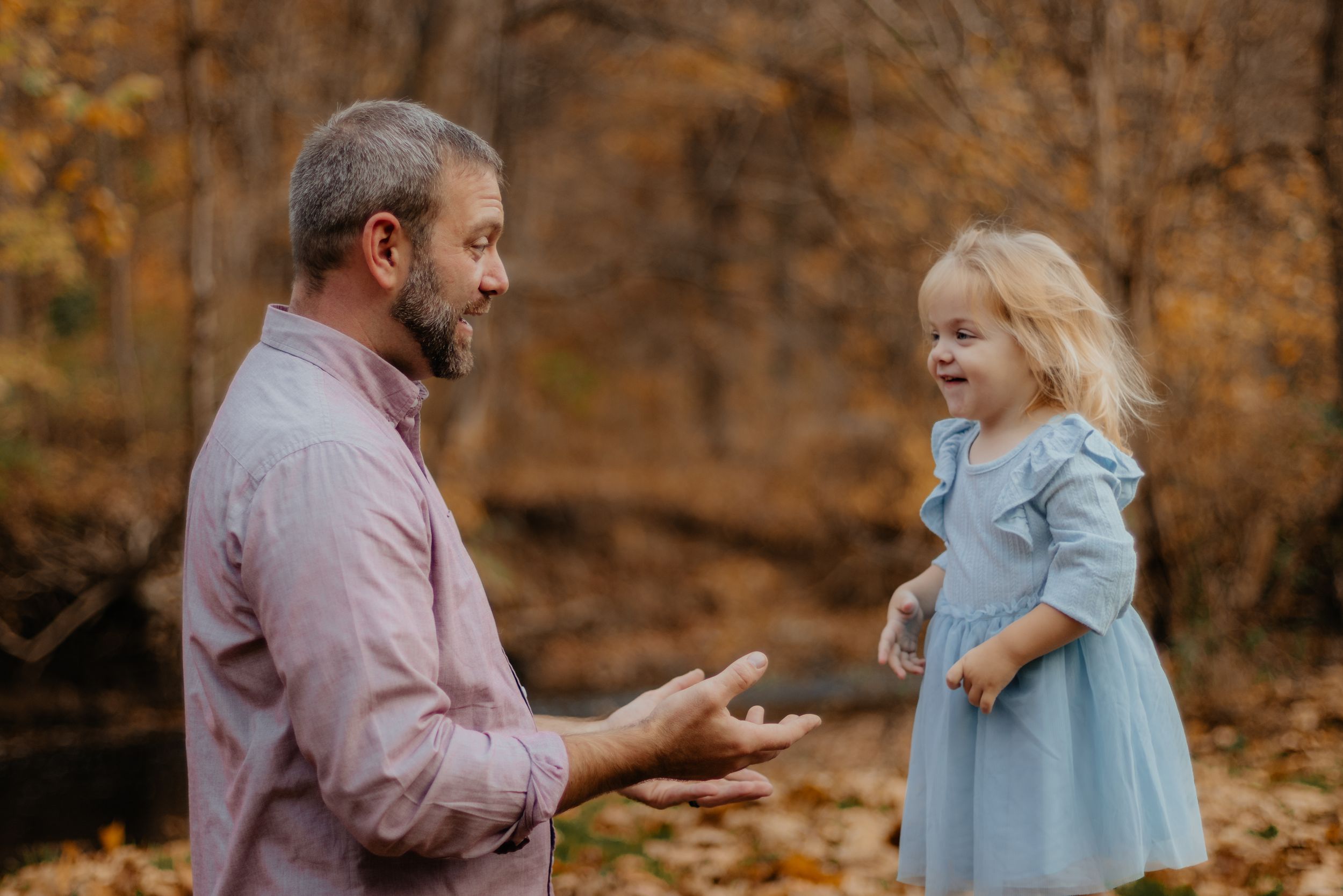 A playful autumn photoshoot in a wooded area with warm golden tones and fallen leaves.