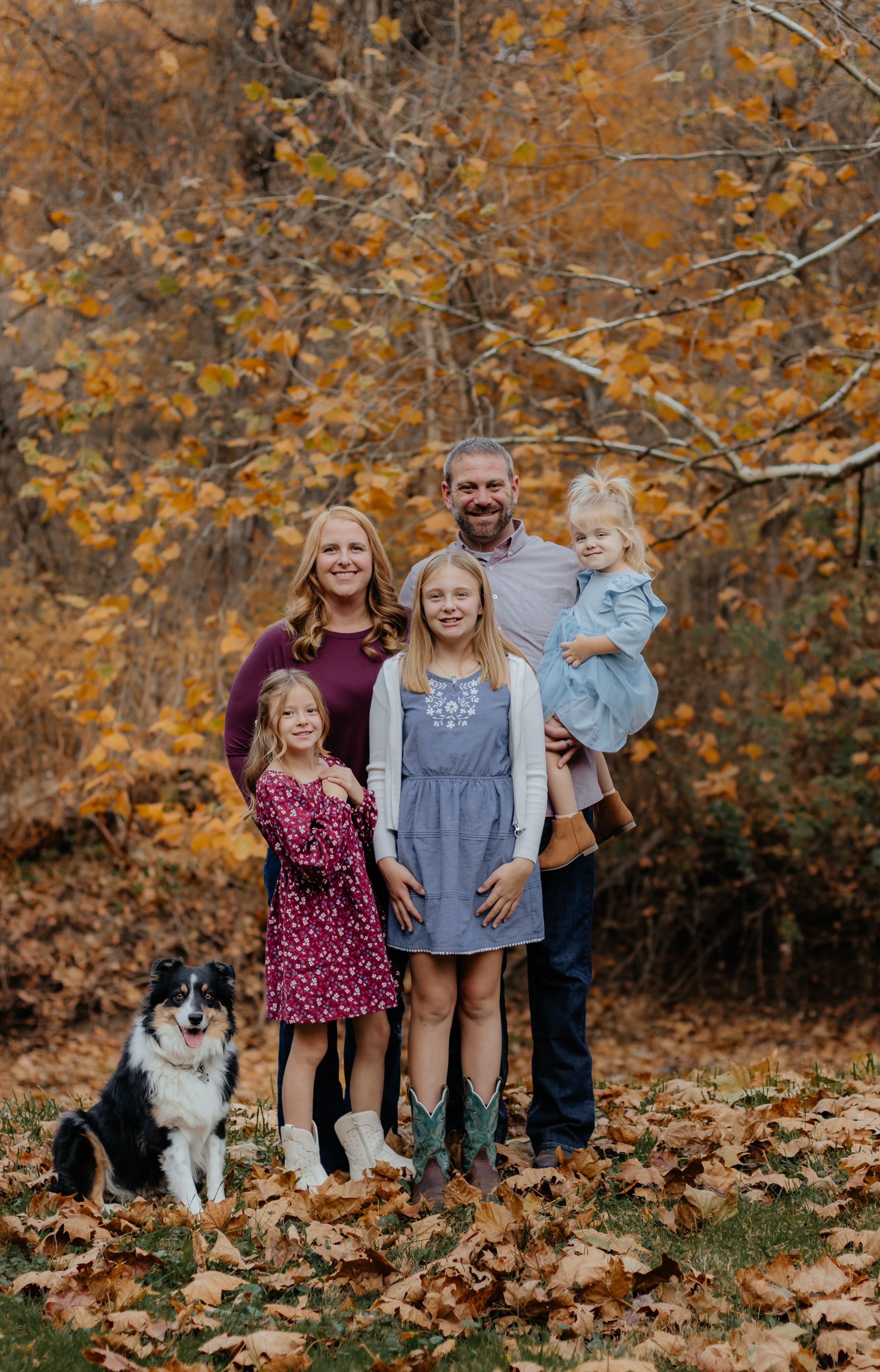 Family group photo with pet dog surrounded by fallen autumn leaves.