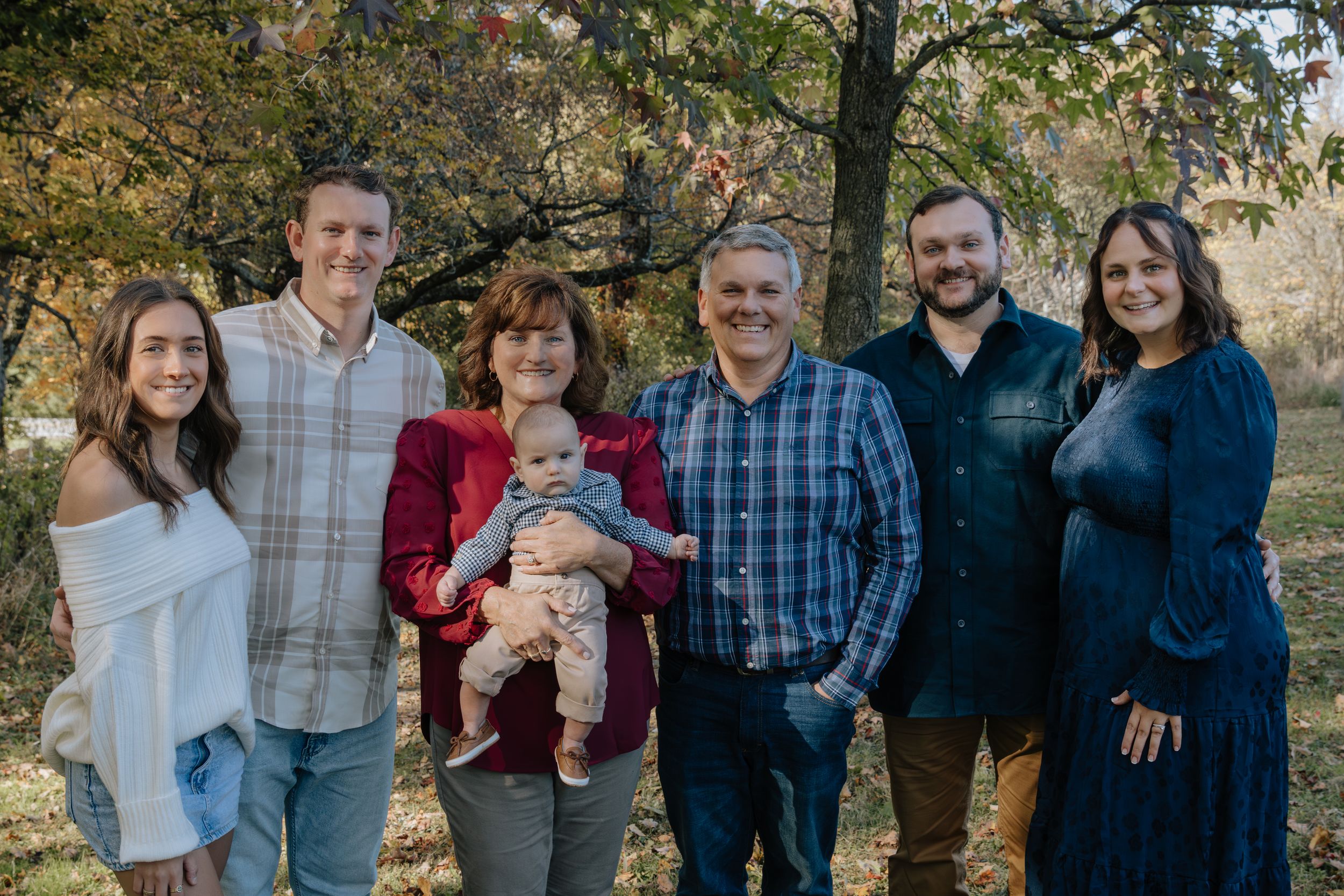 Multi-generational family gathering poses for outdoor portrait in autumn setting.