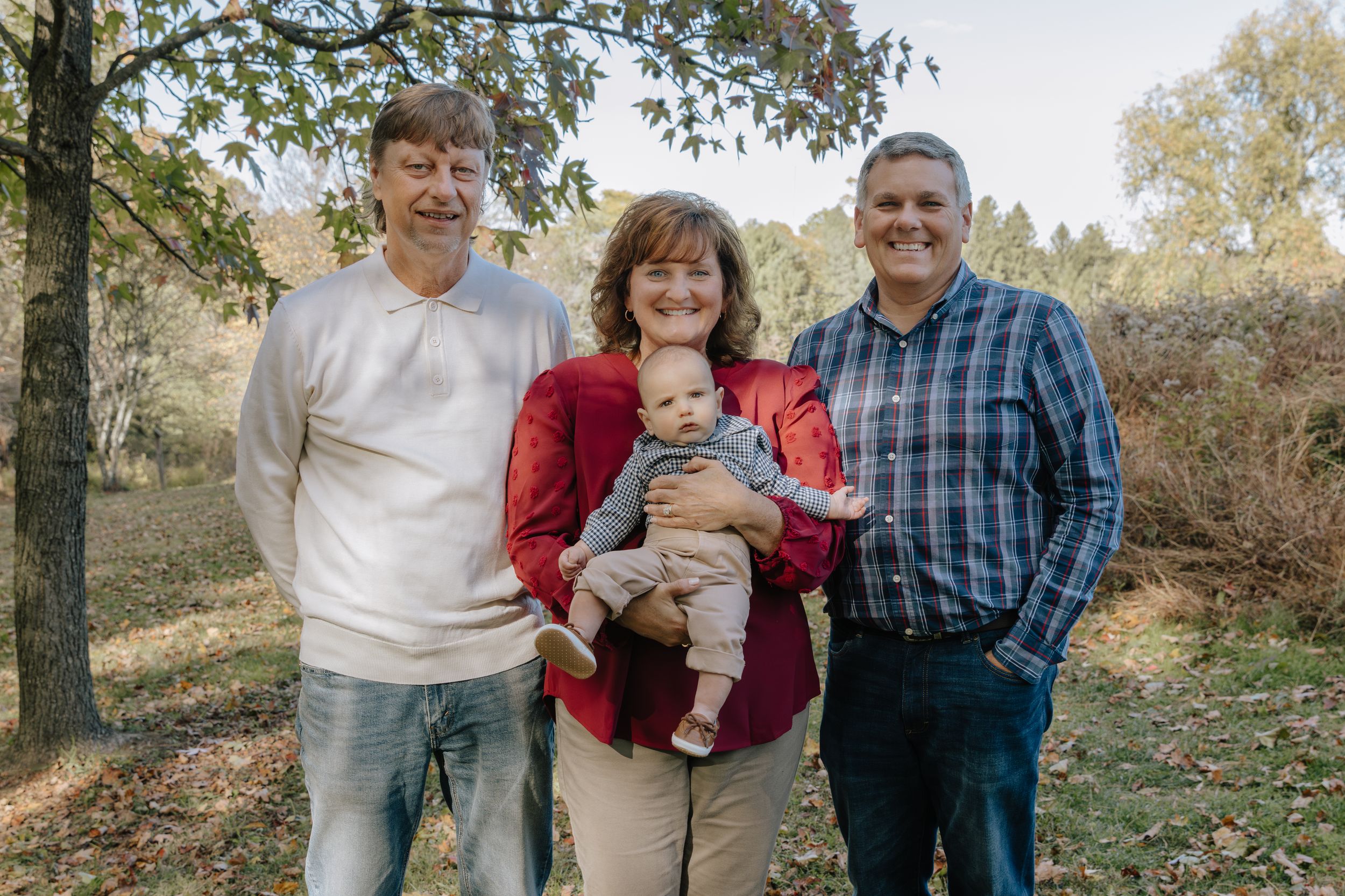 Family members stand together for photo shoot in wooded outdoor setting.