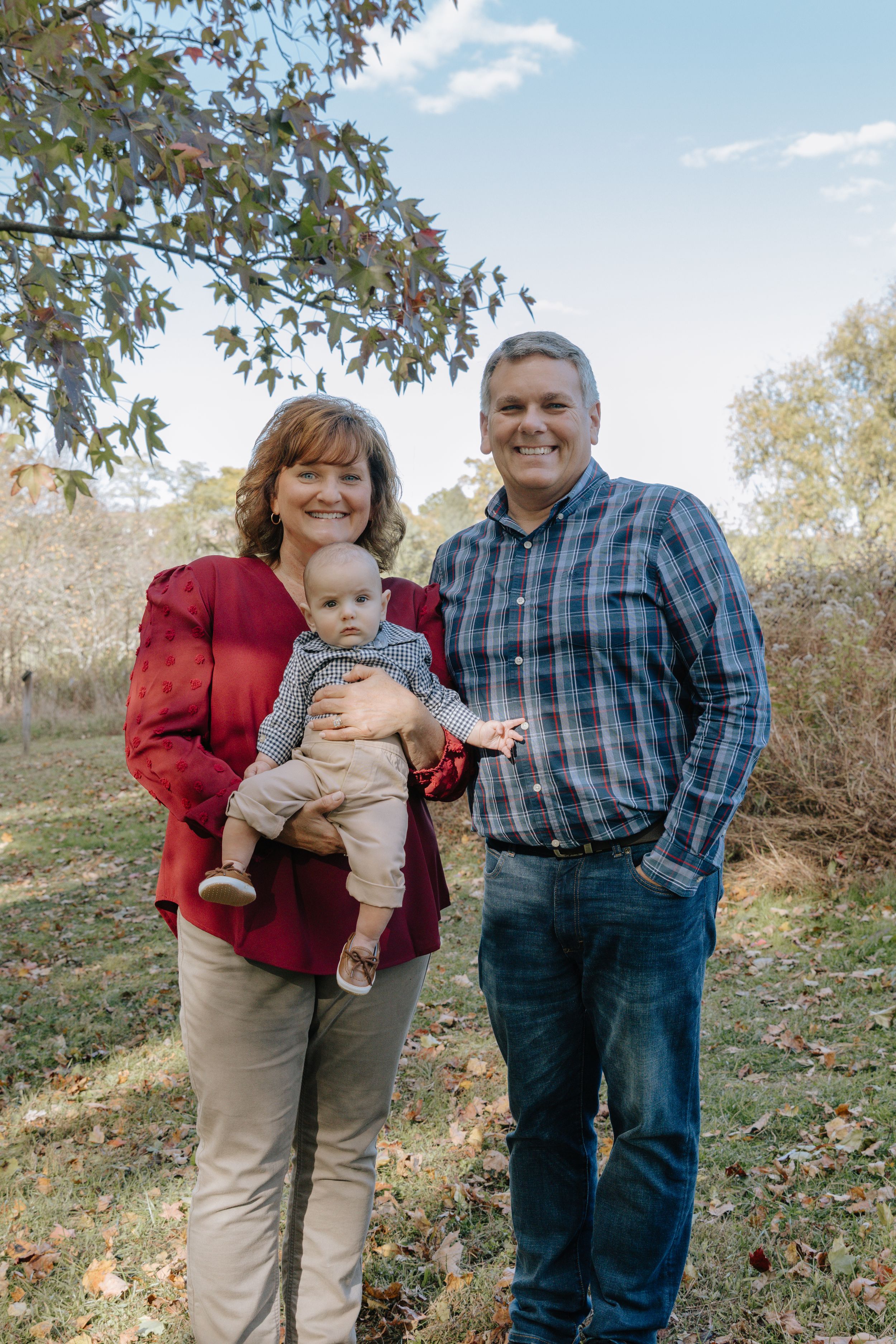 Family members pose together on grassy hillside during fall season.