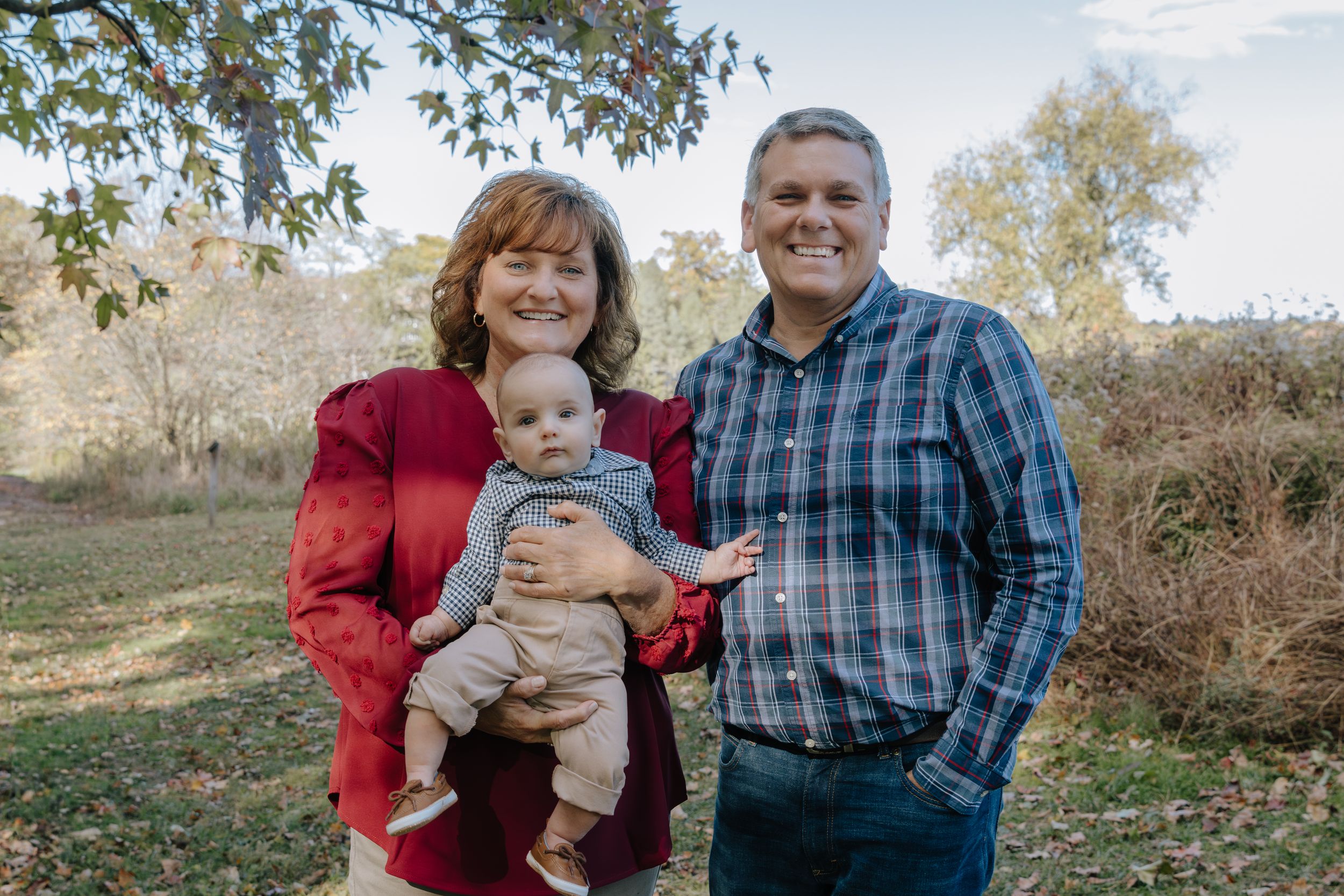 Casual family portrait taken outdoors with autumn trees in background.