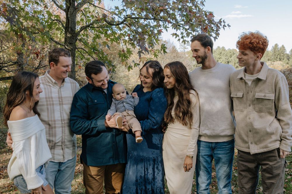 A family poses together outdoors during an autumn photoshoot wearing coordinated casual outfits in neutral tones.
