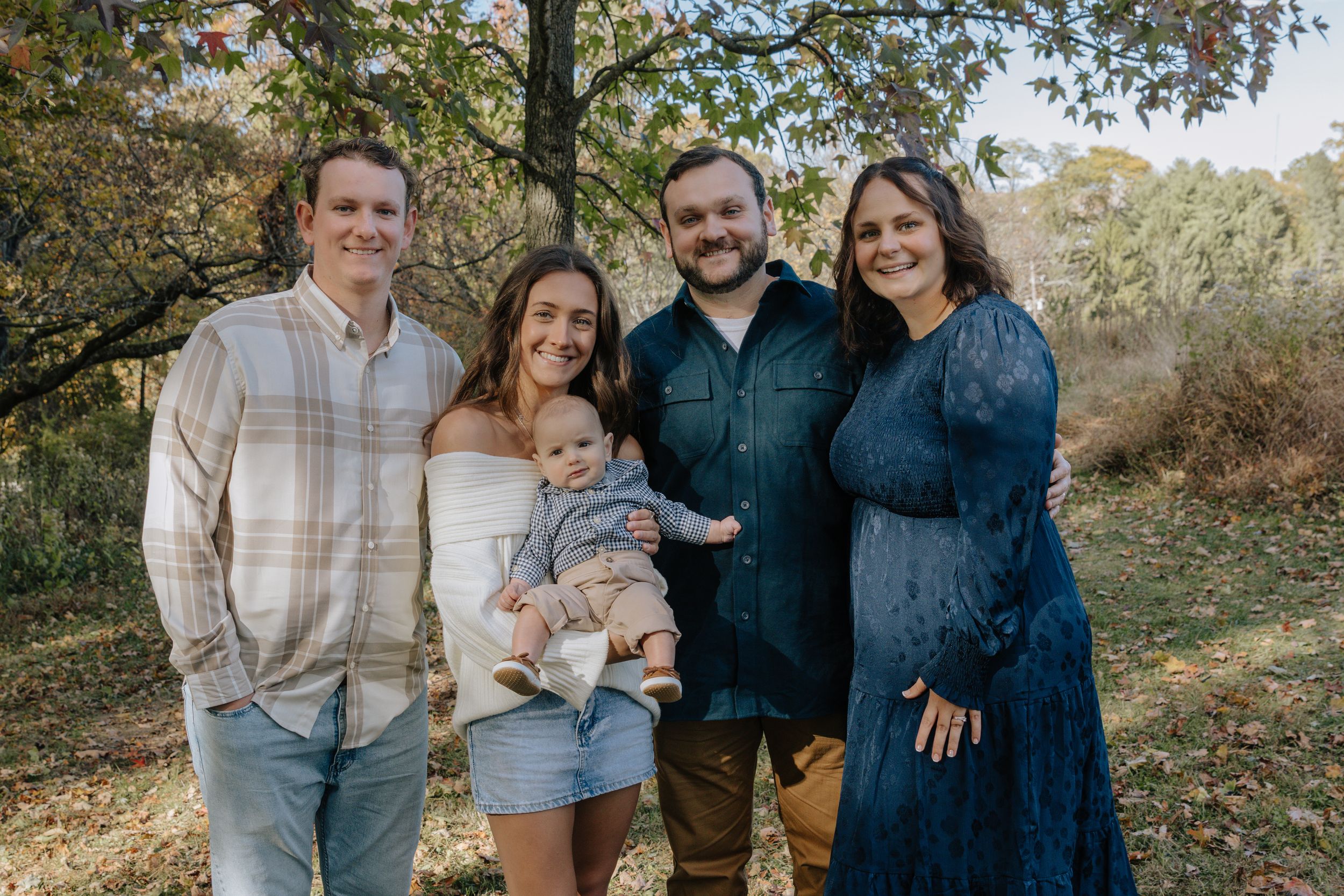Extended family members gather for a casual outdoor portrait session among fall foliage.