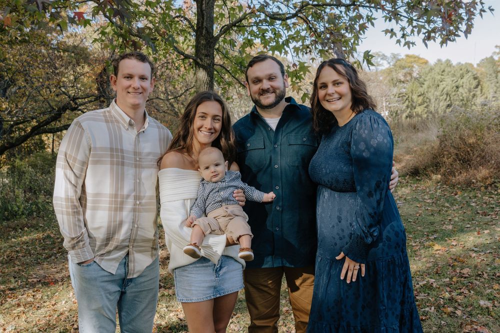 Extended family members gather for a casual outdoor portrait session among fall foliage.