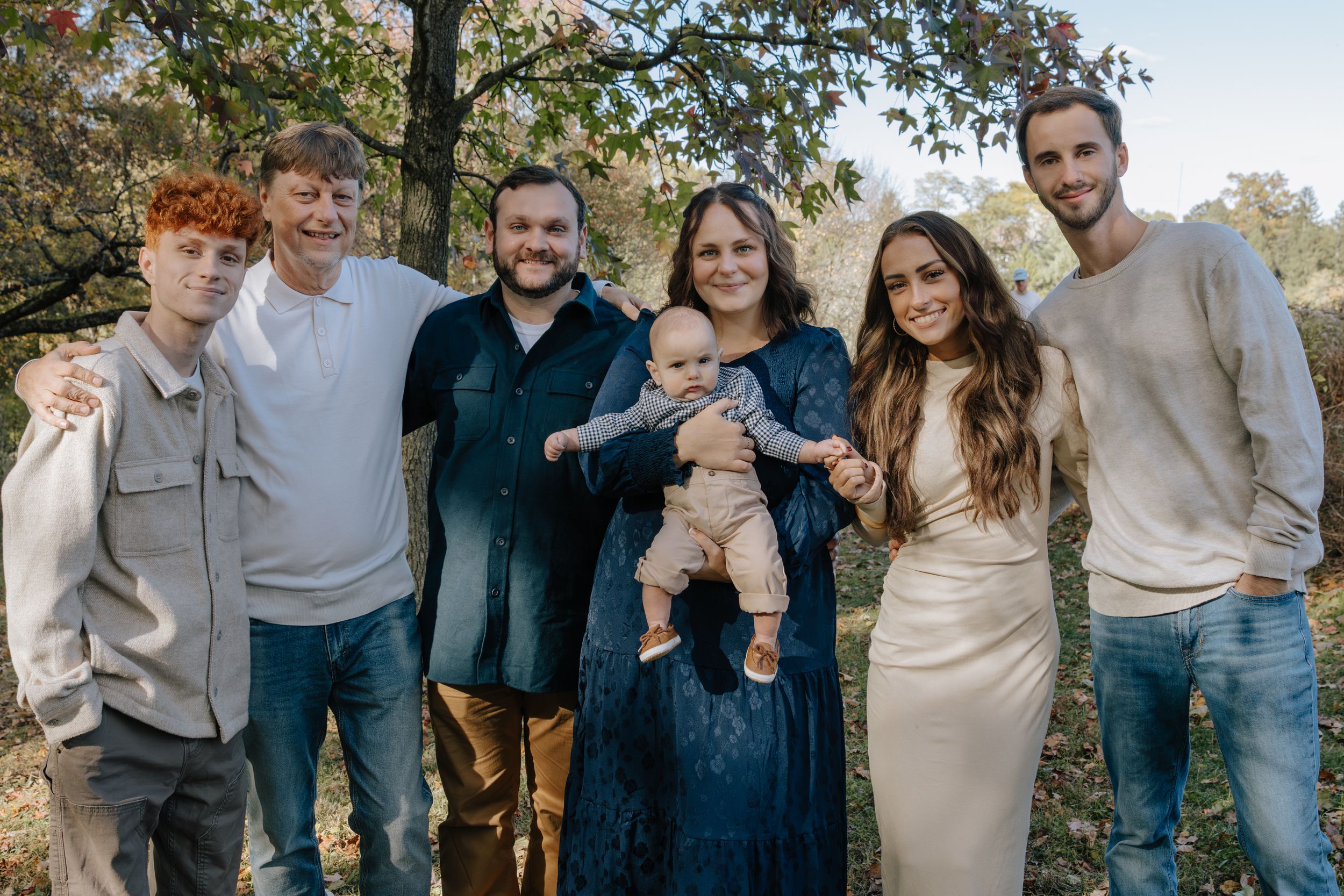 Family members smile together during an outdoor autumn photoshoot with natural scenery.