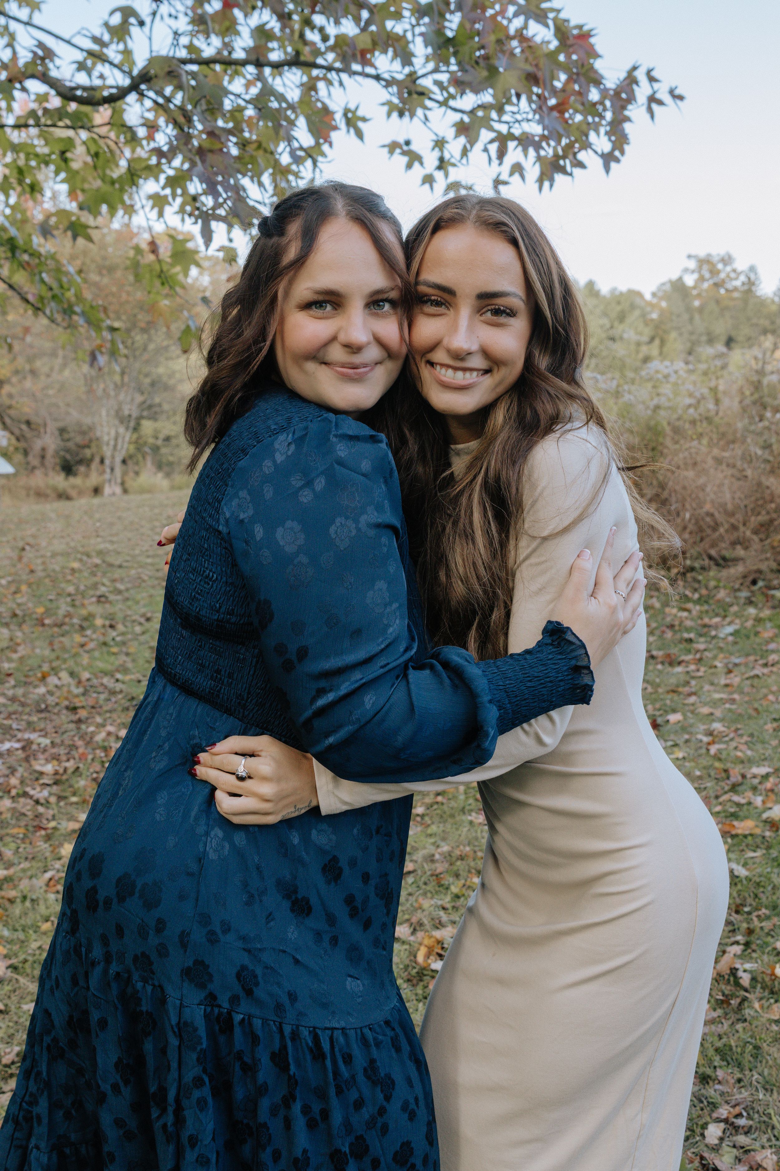 Two people embrace while wearing contrasting navy and beige dresses outdoors.