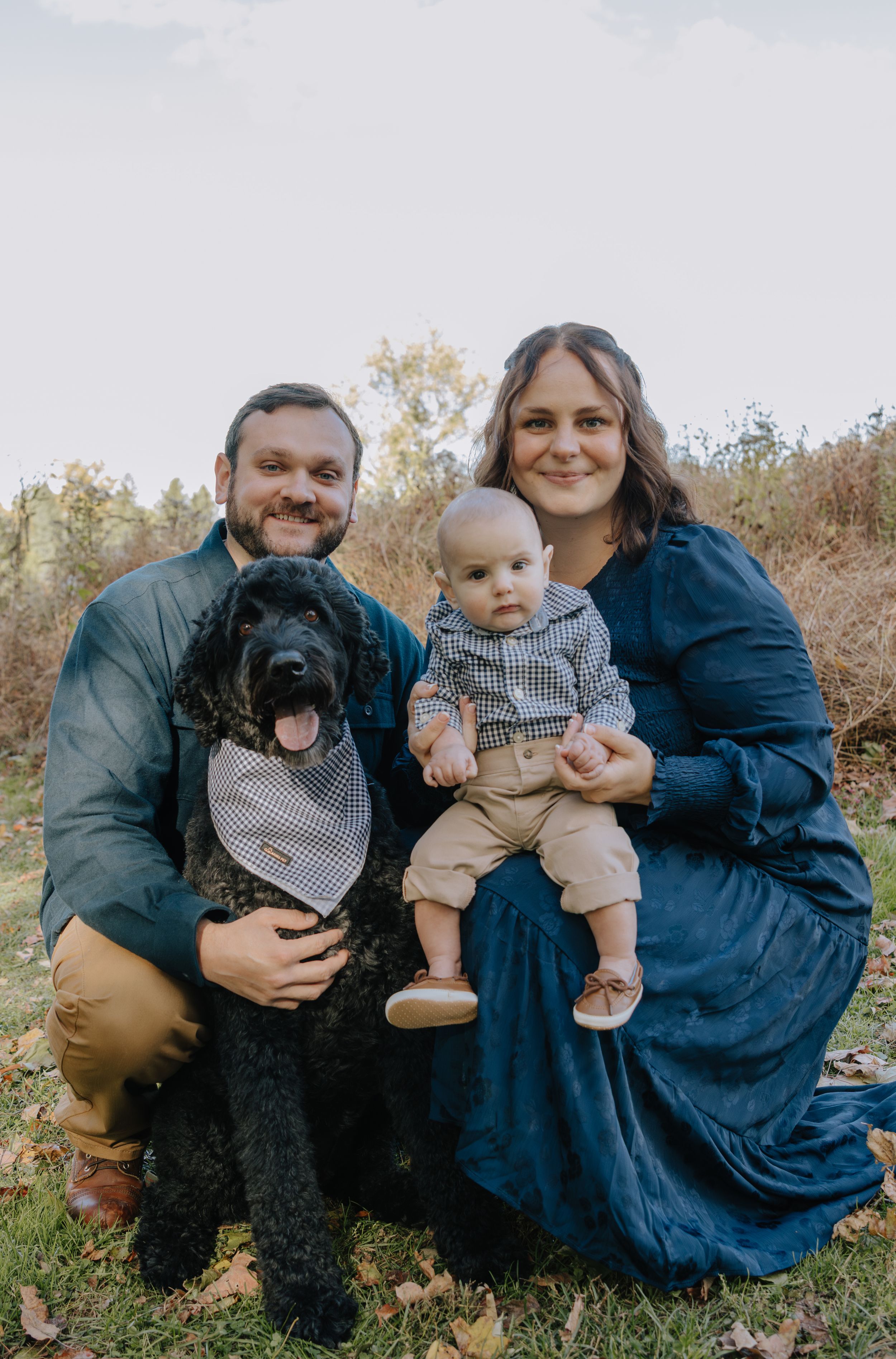 Family poses with their infant and black dog during casual outdoor autumn photoshoot.