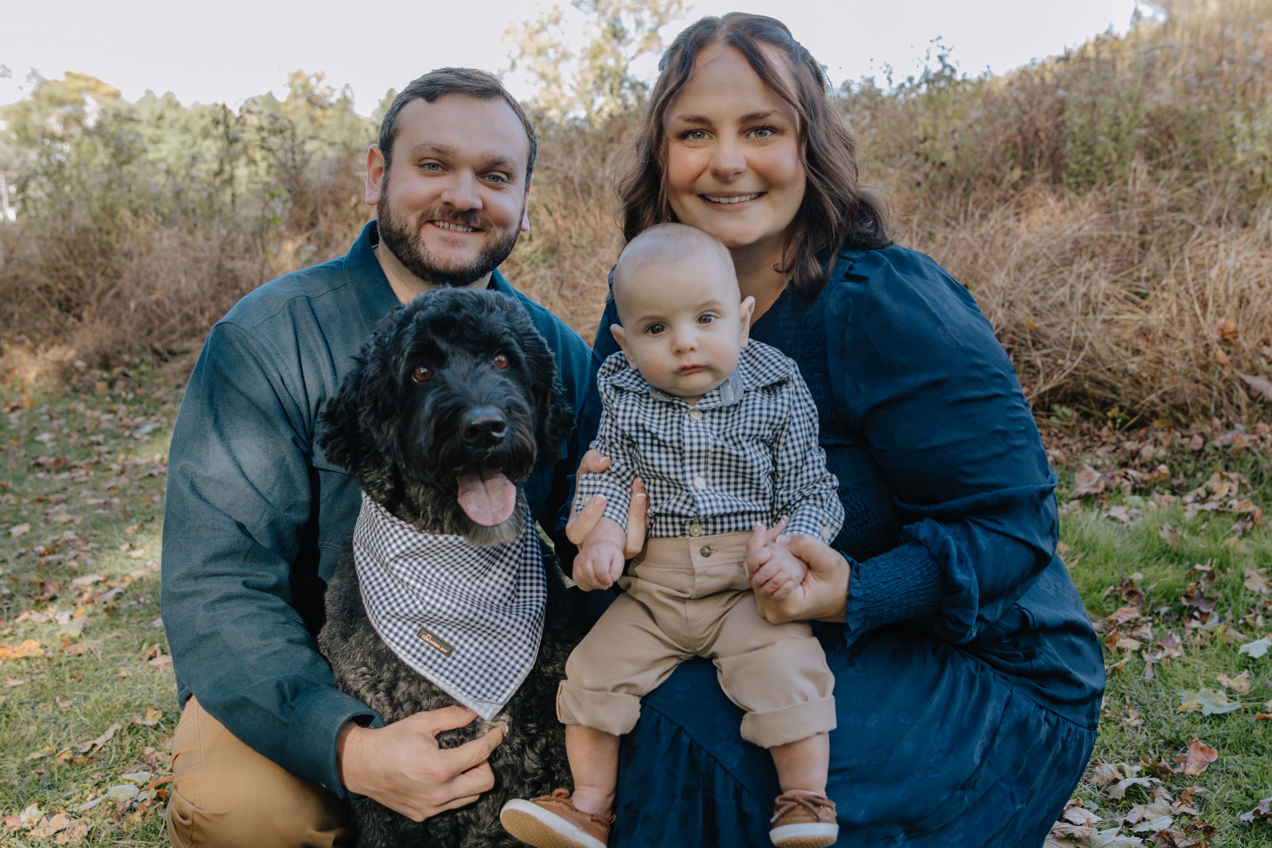 Family group sits together with baby and pet dog during outdoor portrait session.
