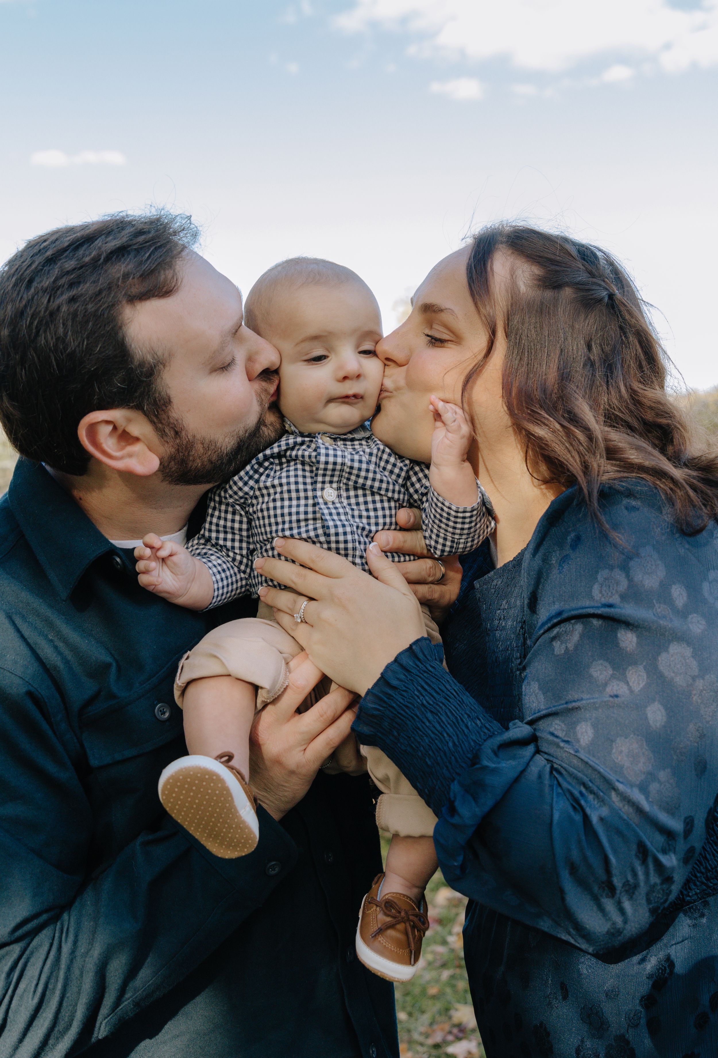 A family shares tender kisses with their baby outdoors against a natural backdrop.