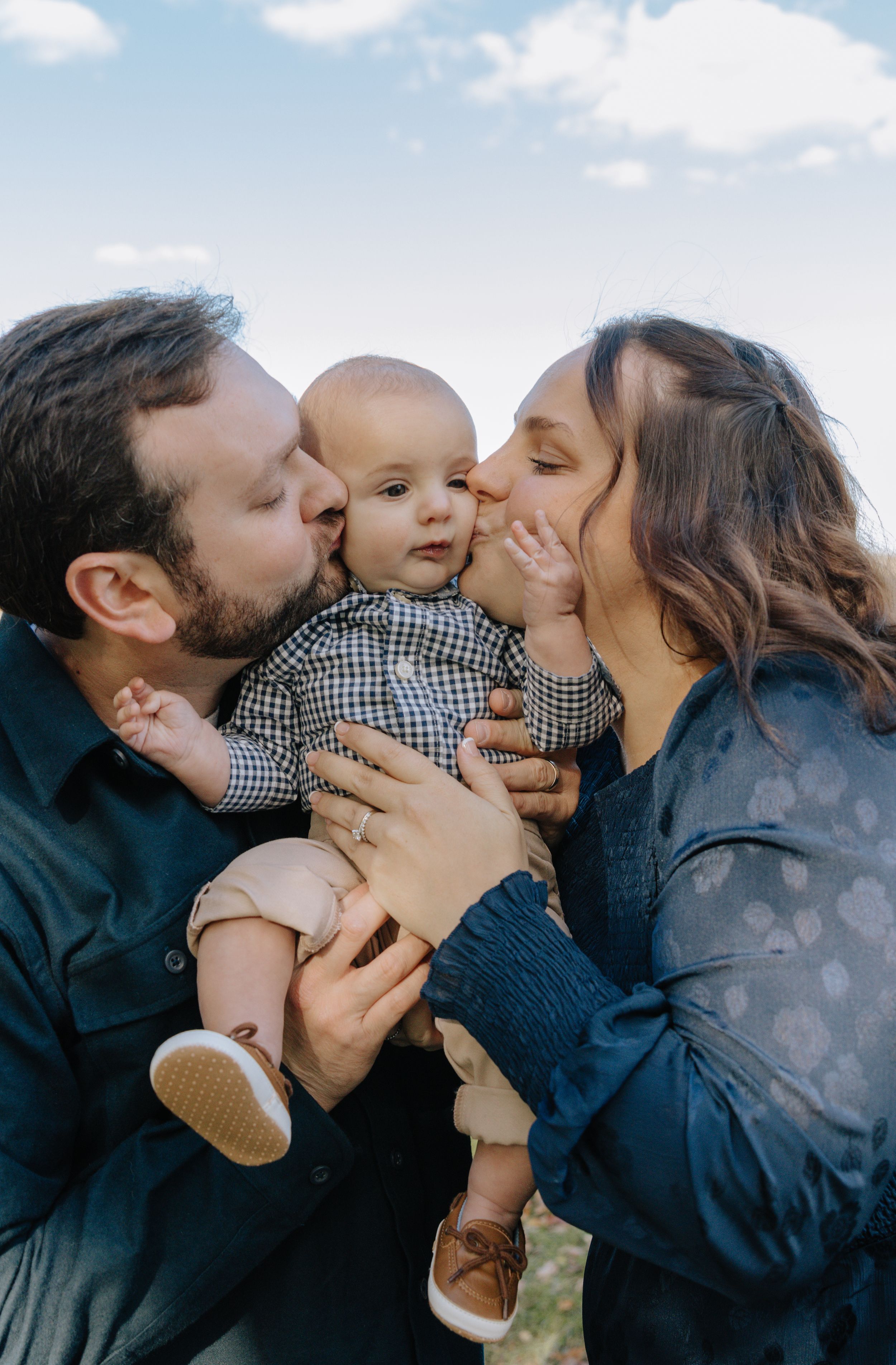 Parents showering their baby with affection in a sweet outdoor family moment.
