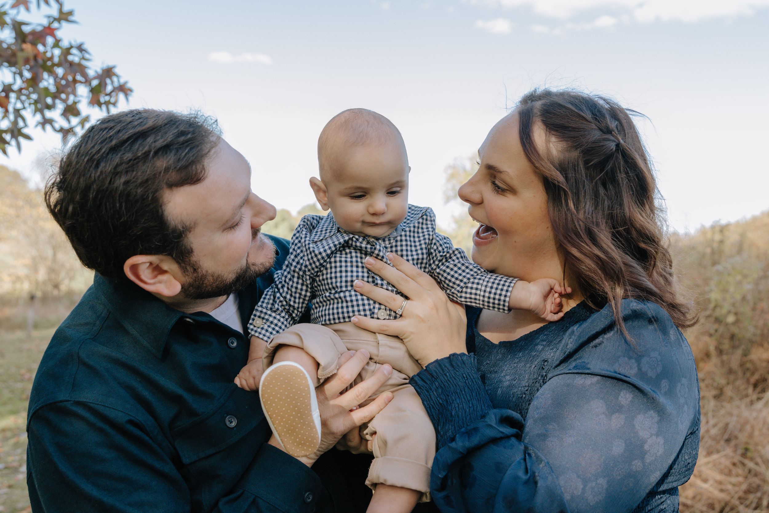 A loving family moment captured outdoors with parents kissing their young child.