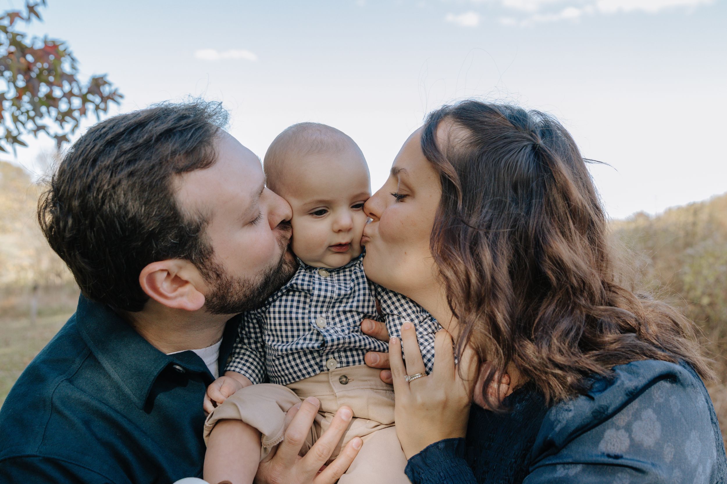 Family sharing joyful kisses and cuddles with their baby in a natural setting.