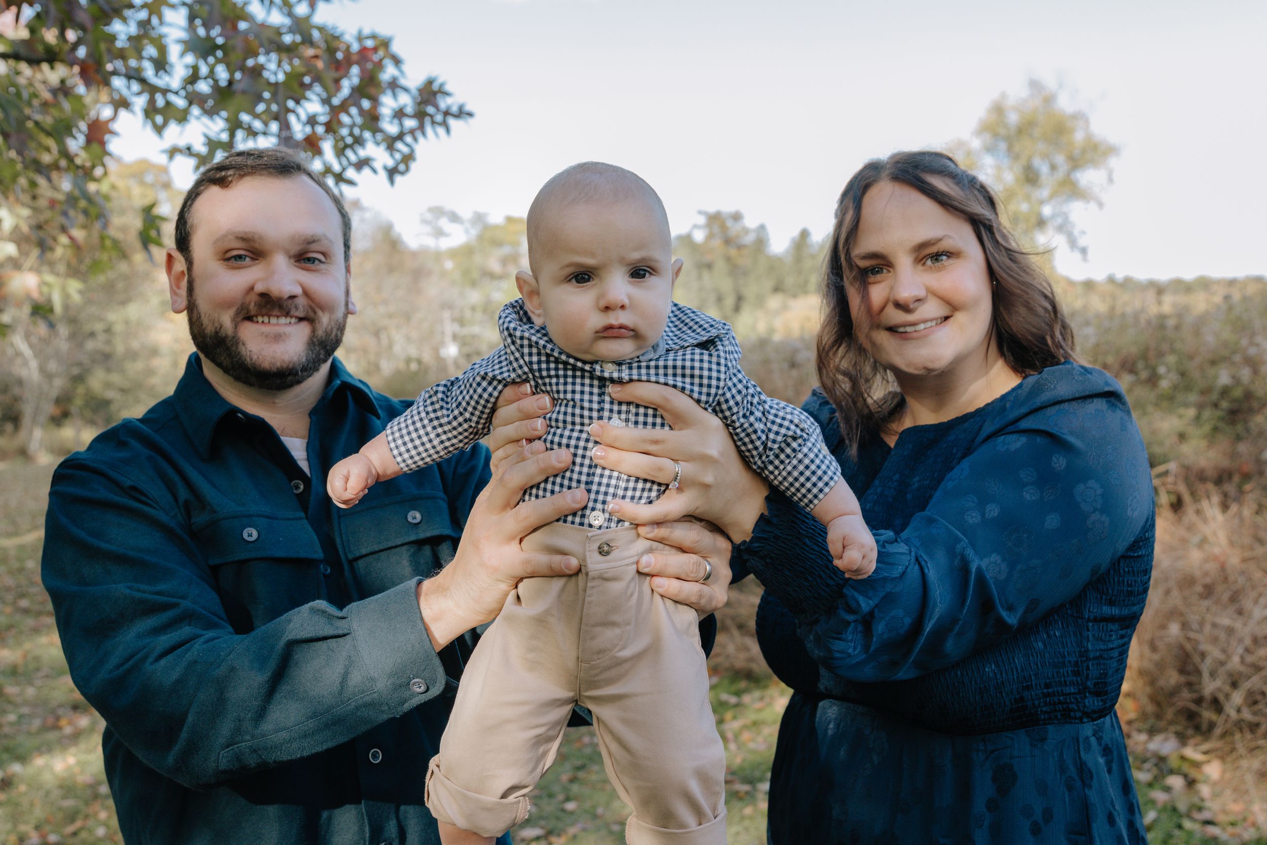 Outdoor family photoshoot capturing playful moments between parents and baby.