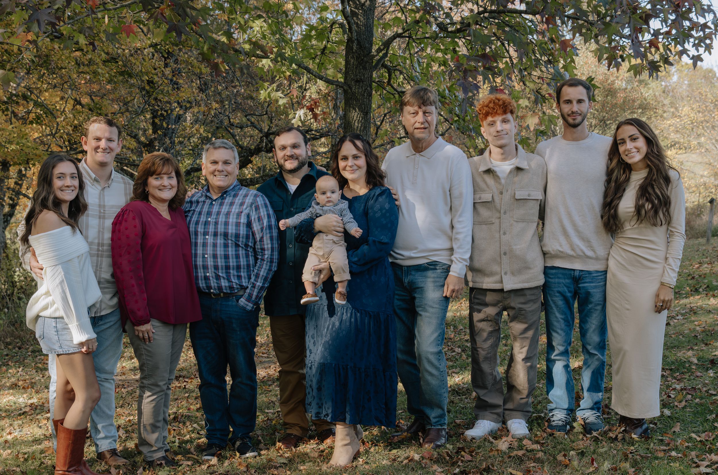 Large family group poses together under autumn trees for outdoor portrait.