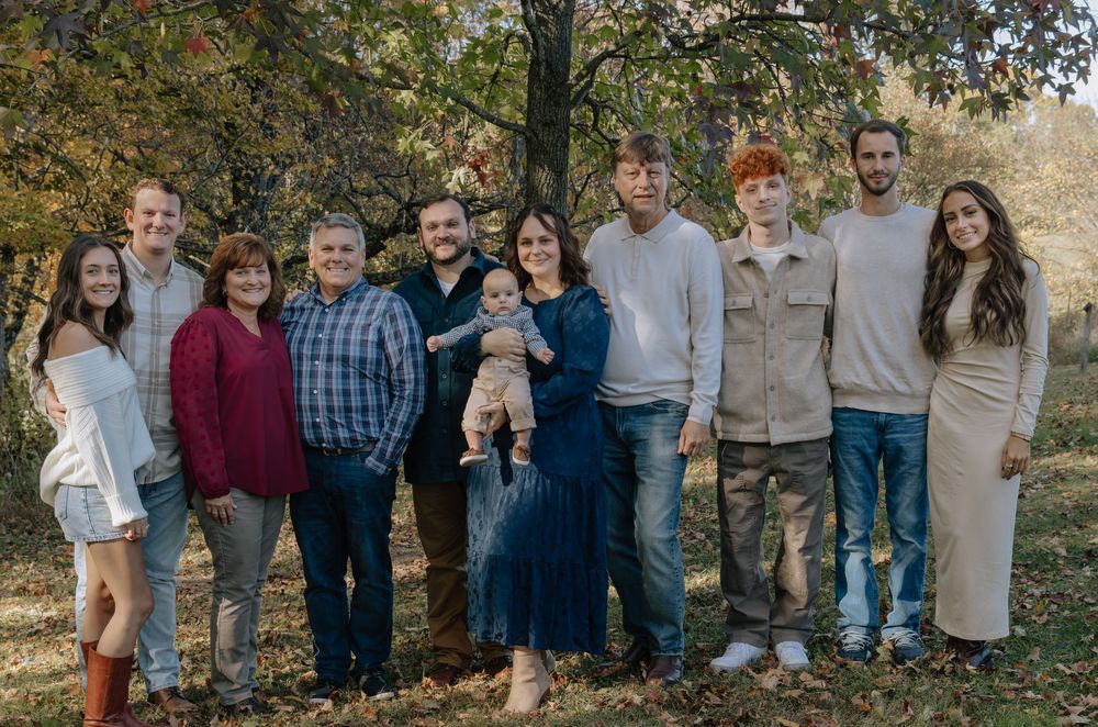 Large family group poses together under autumn trees for outdoor portrait.