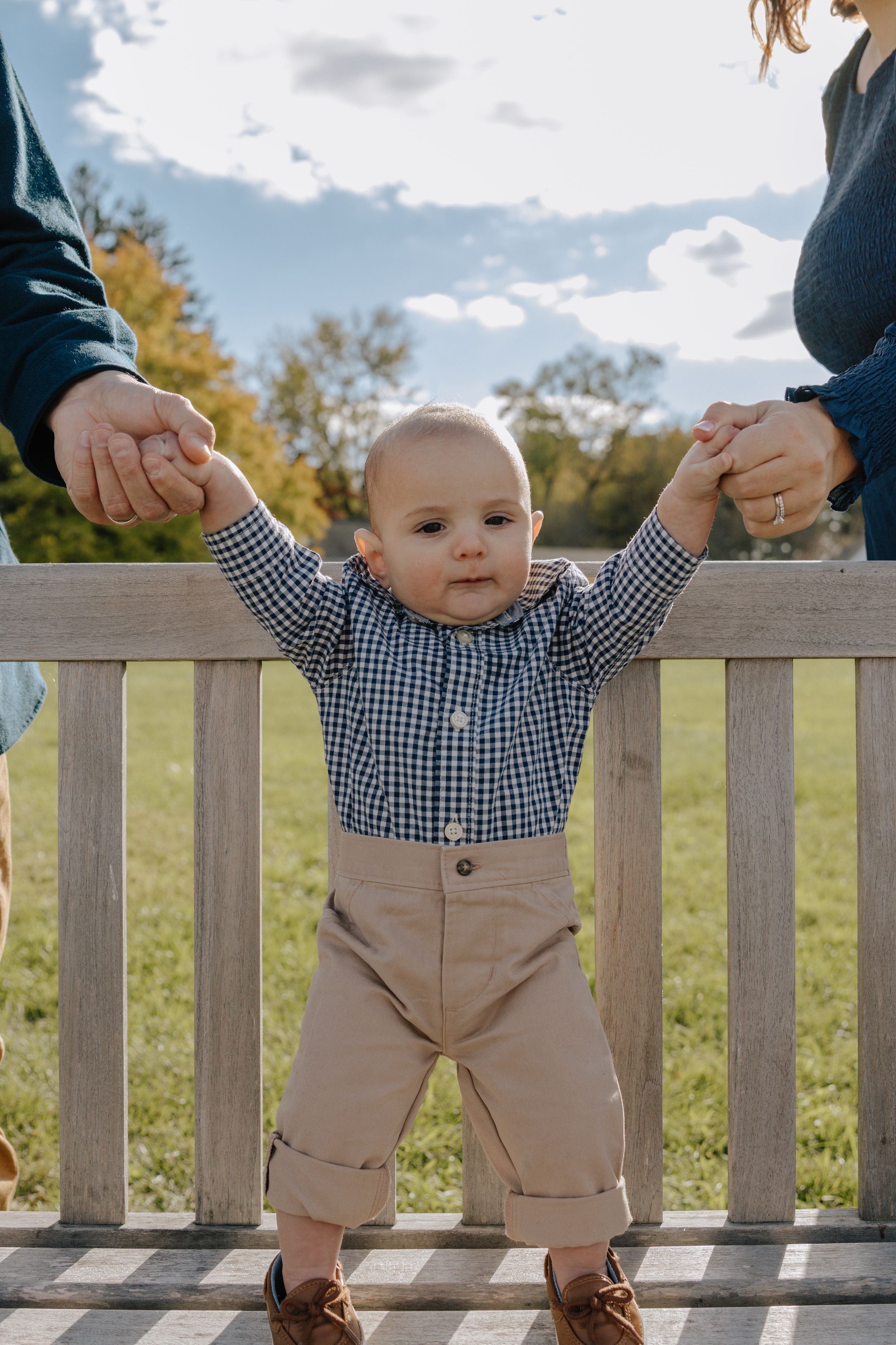 Small child standing against white fence railing in countryside setting.