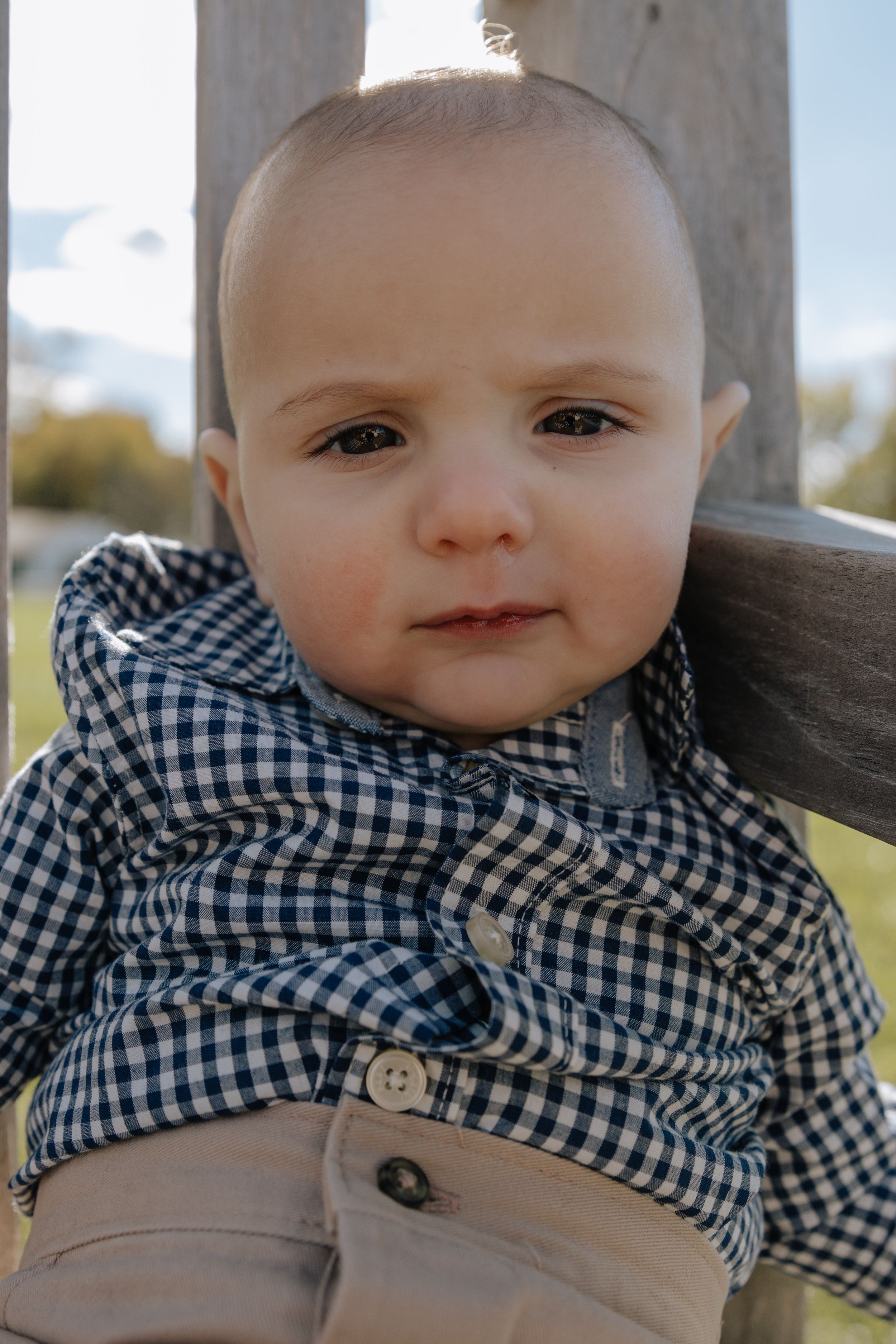 Close up of baby wearing black and white gingham shirt against wooden fence.