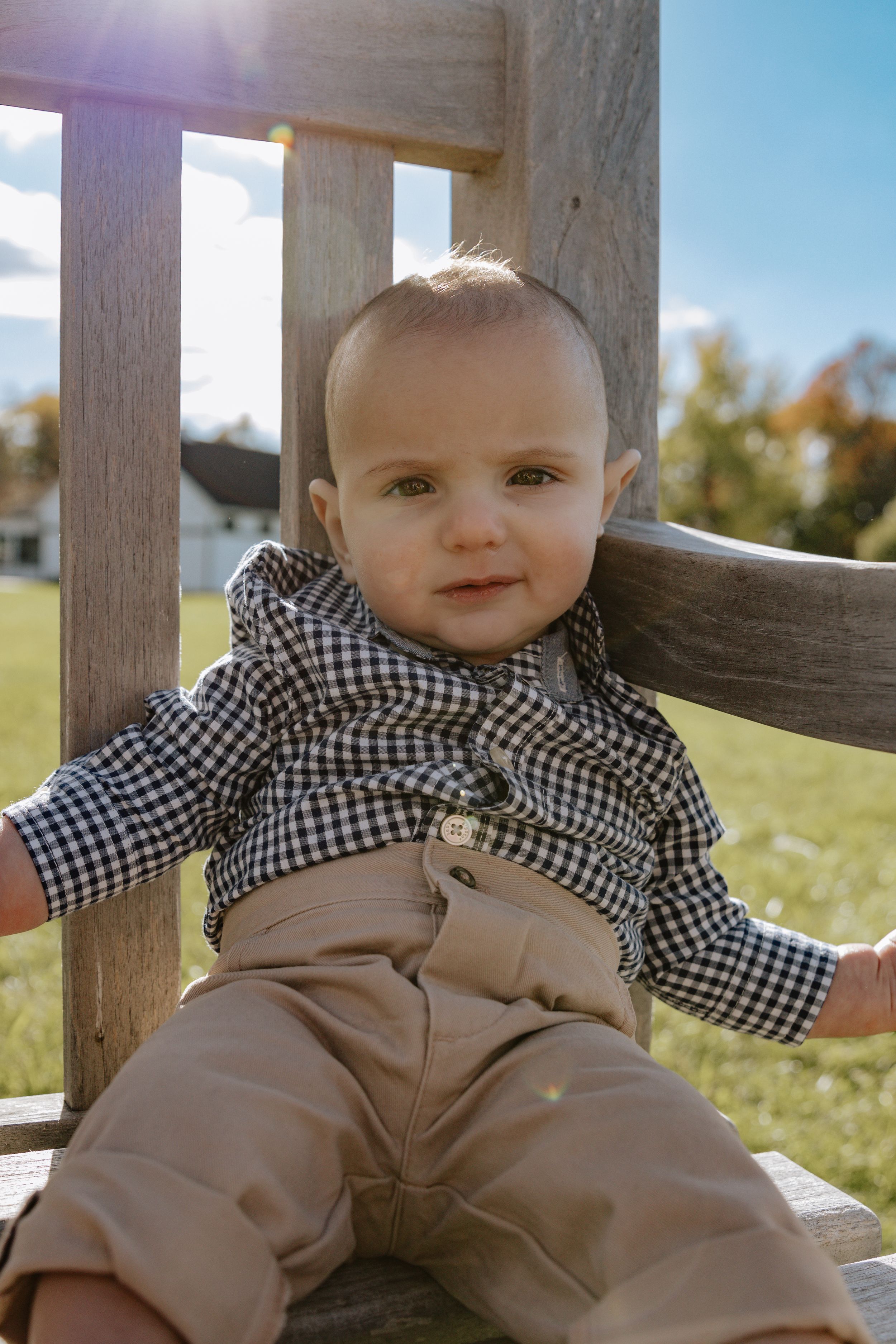 Baby in casual outfit sitting on wooden fence rail on sunny day.
