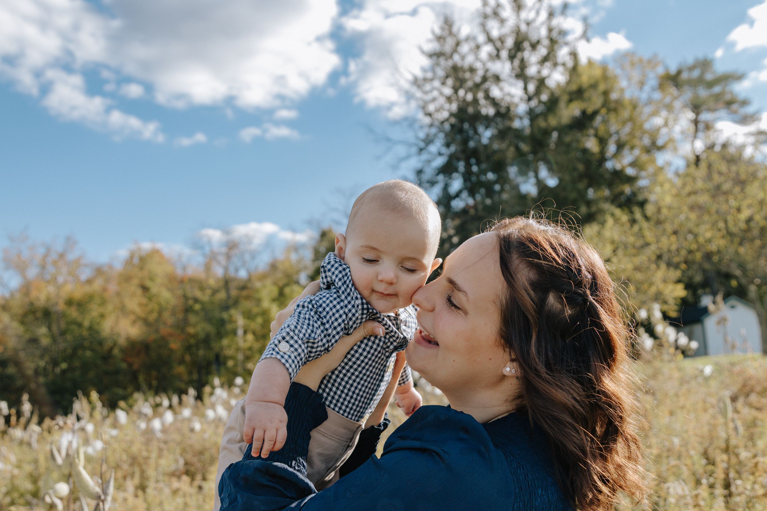 Parent and baby share a playful moment in a sunny meadow with wildflowers.