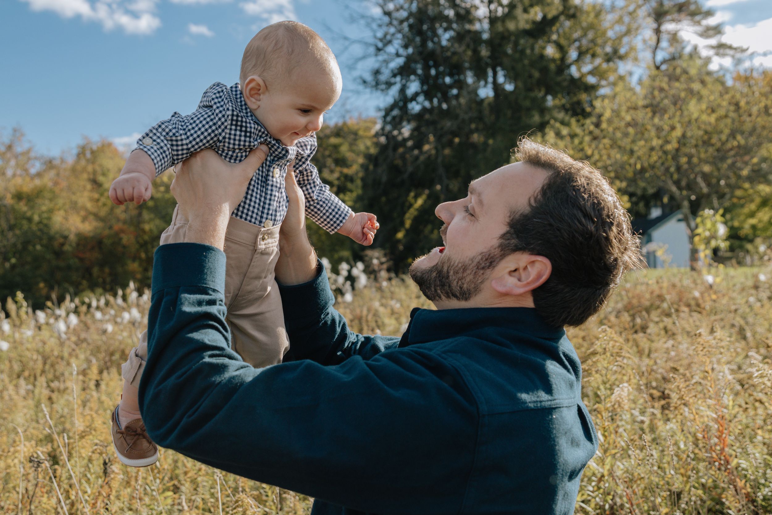 Parent lifts baby high in the air during playful outdoor moment.