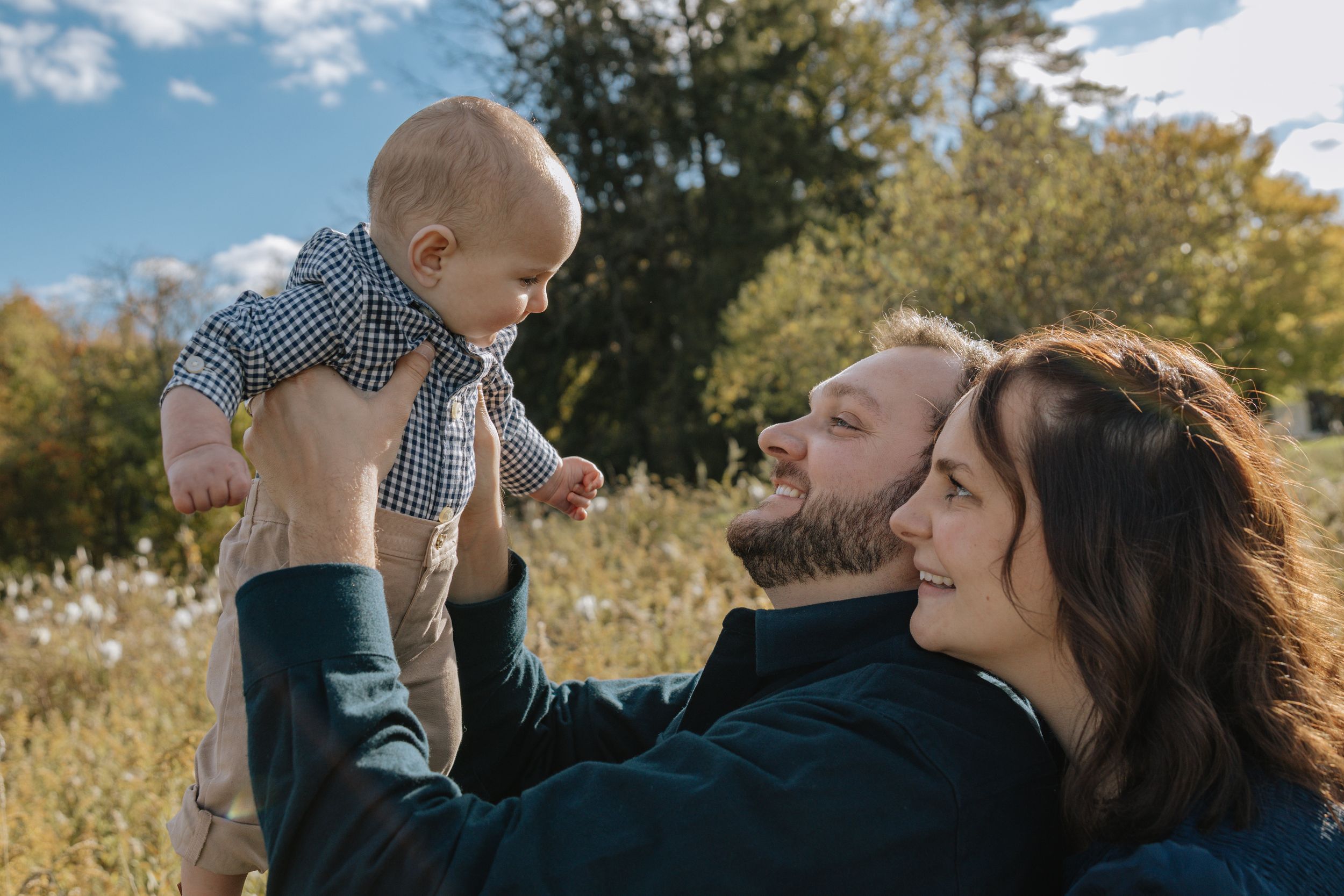 Family shares joyful moment lifting baby in autumn field setting.