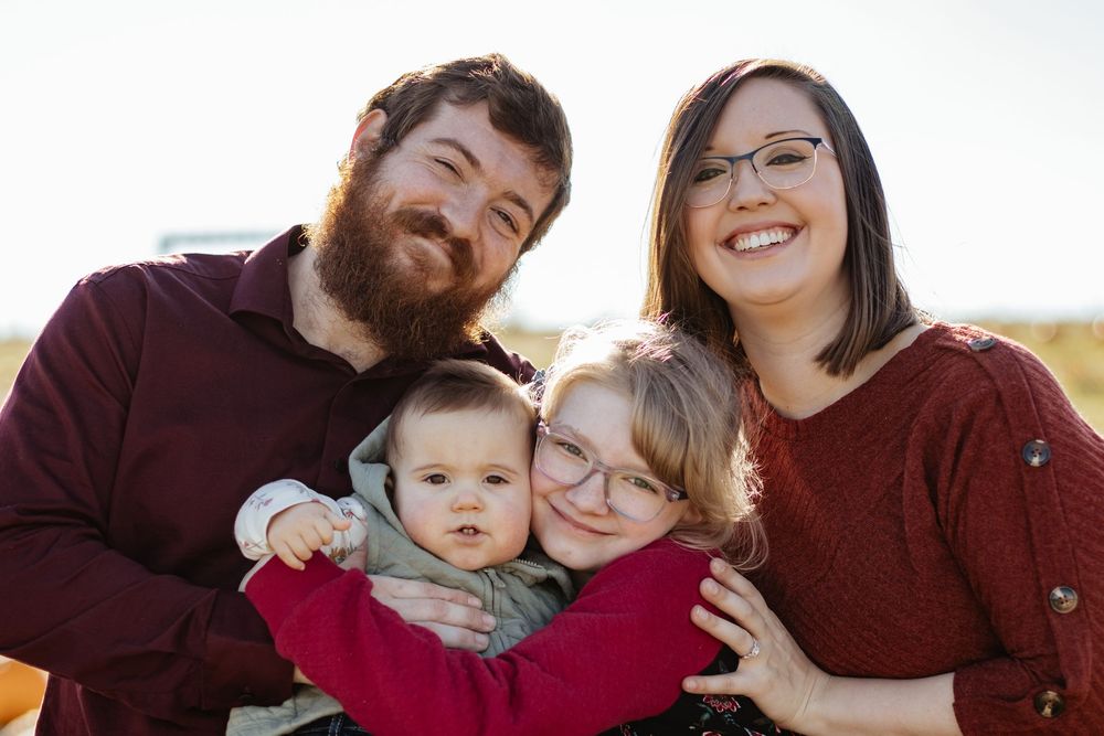 An intimate family portrait captured against a bright white background outdoors.