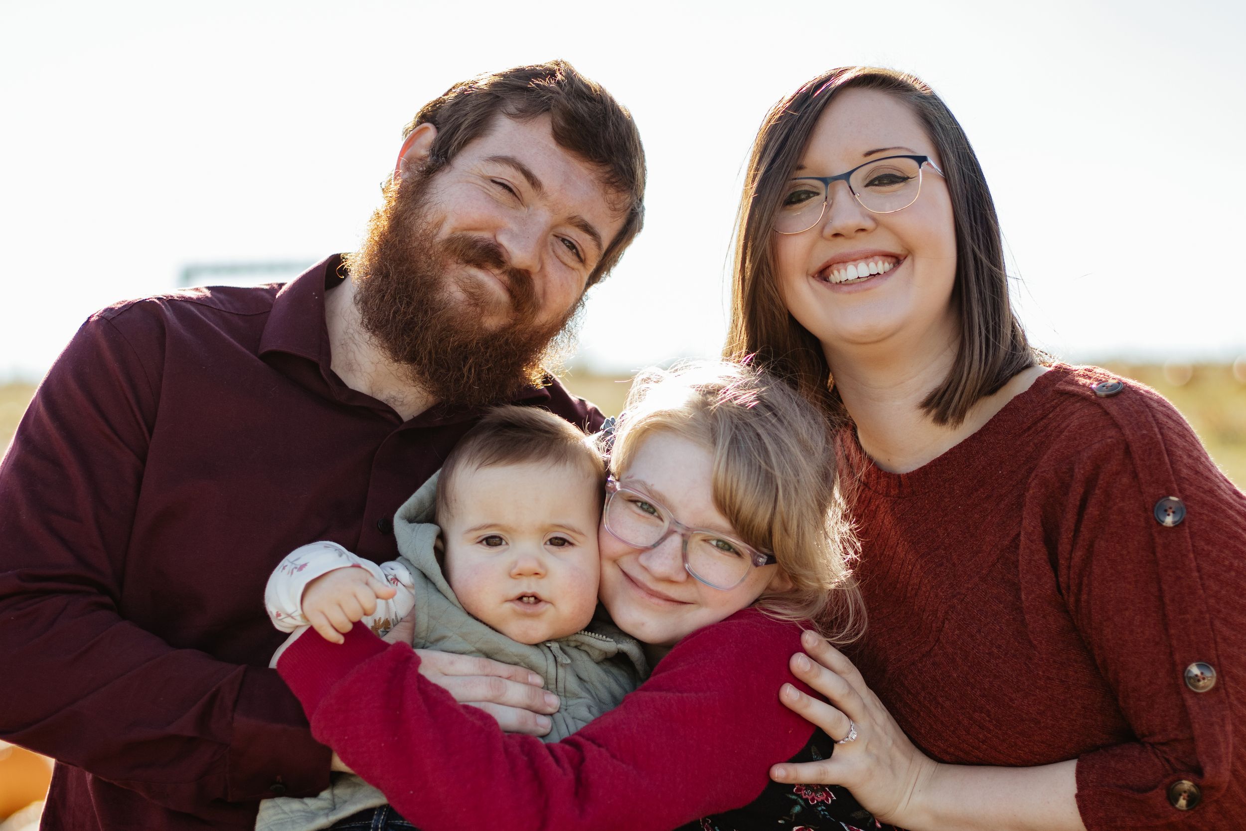 An intimate family portrait captured against a bright white background outdoors.