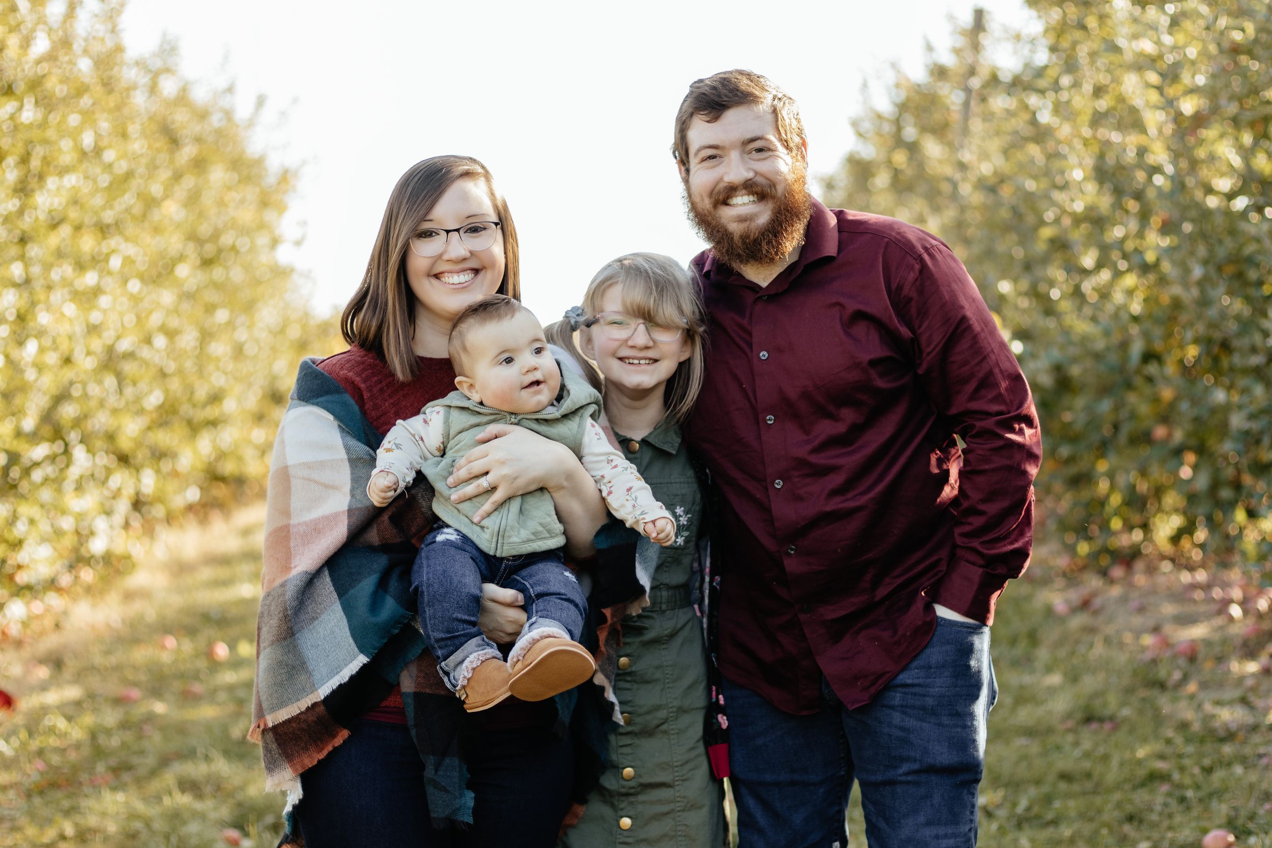 A candid family photo session in a sun-lit field with golden fall foliage.