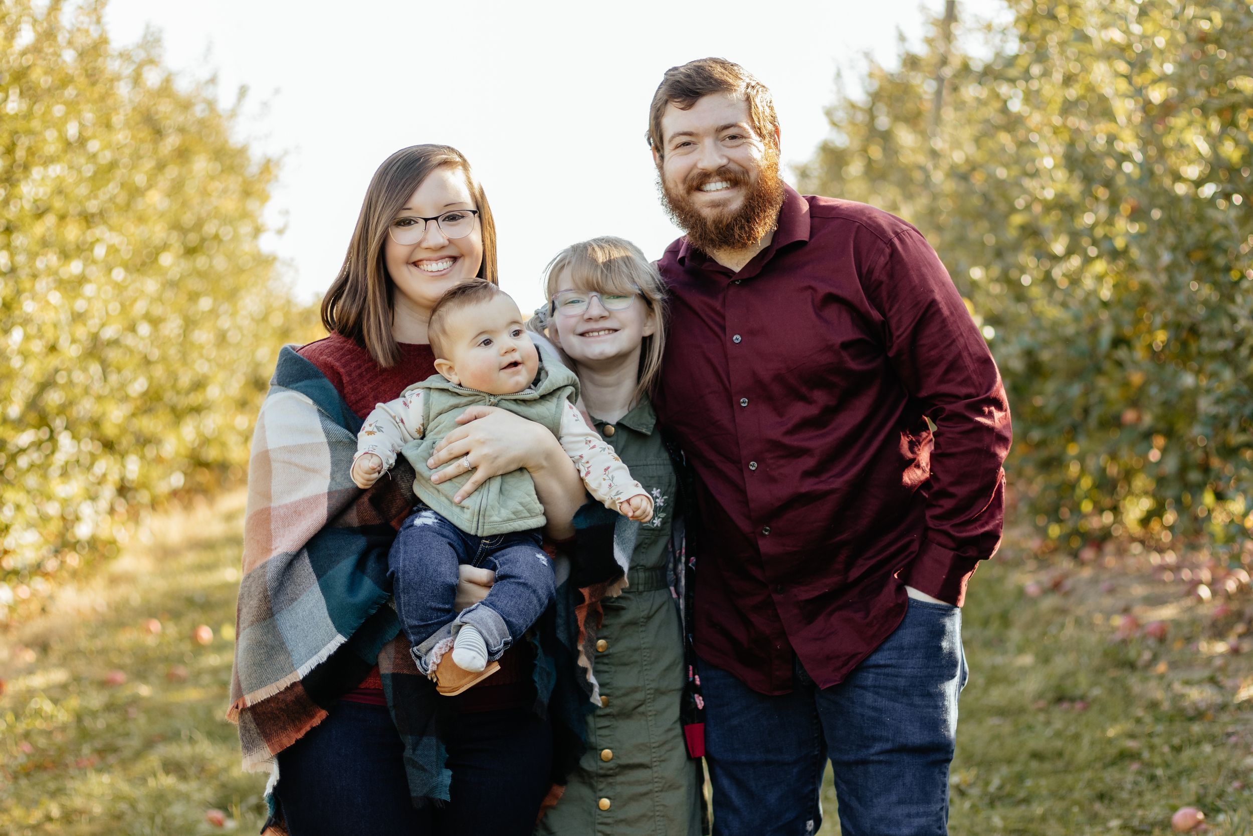 A relaxed outdoor family portrait with natural autumn scenery in the background.