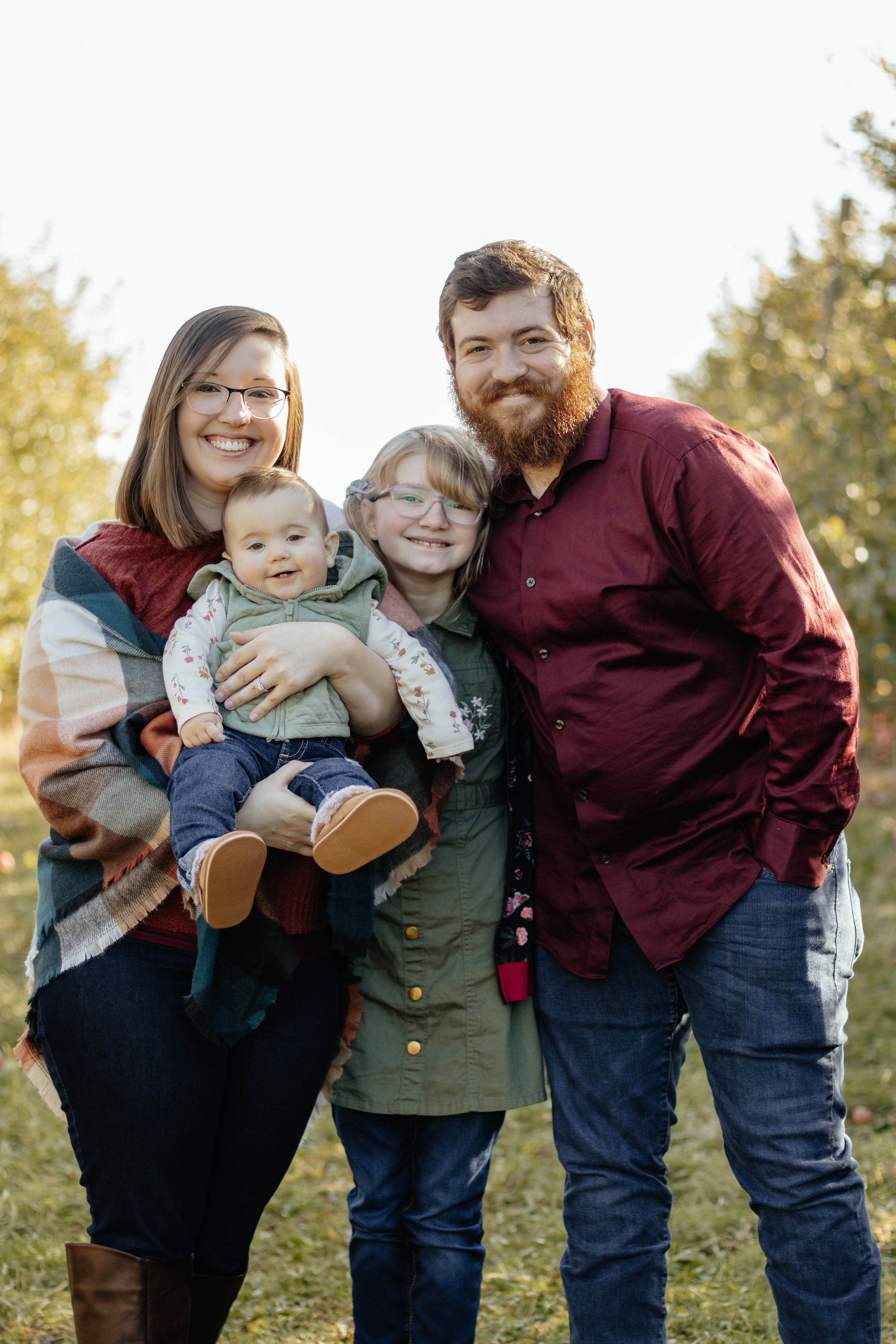 A cheerful family group poses together on a grassy hill during golden hour.
