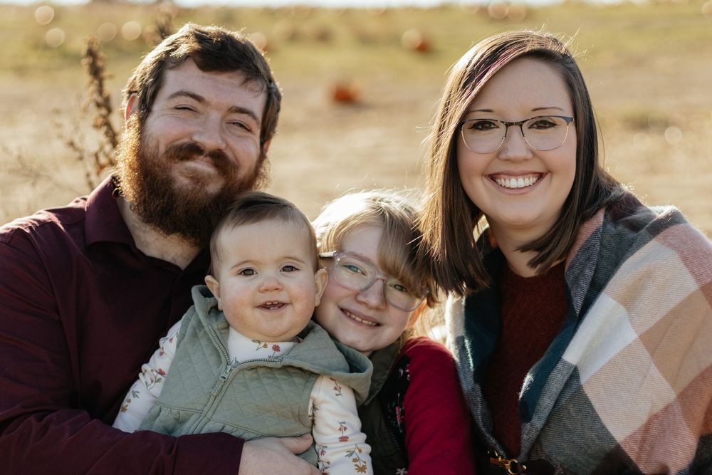 A casual outdoor family portrait session in a golden field during sunset.