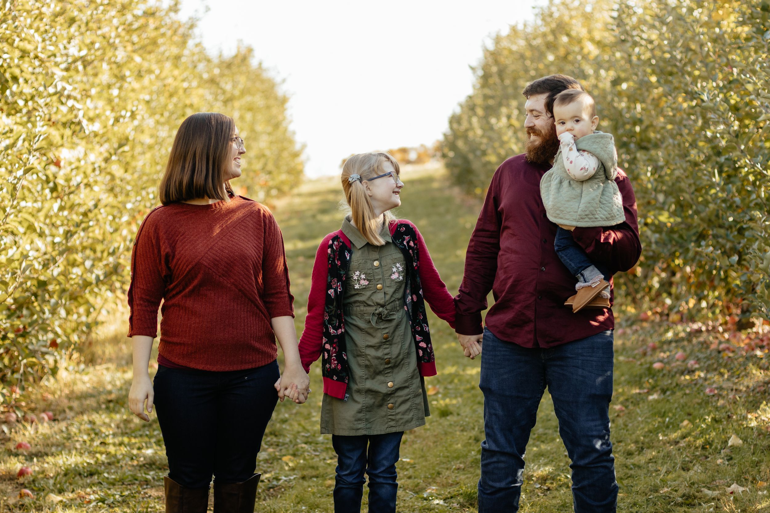 Family walking together during fall photo session with sunlit trees in background.