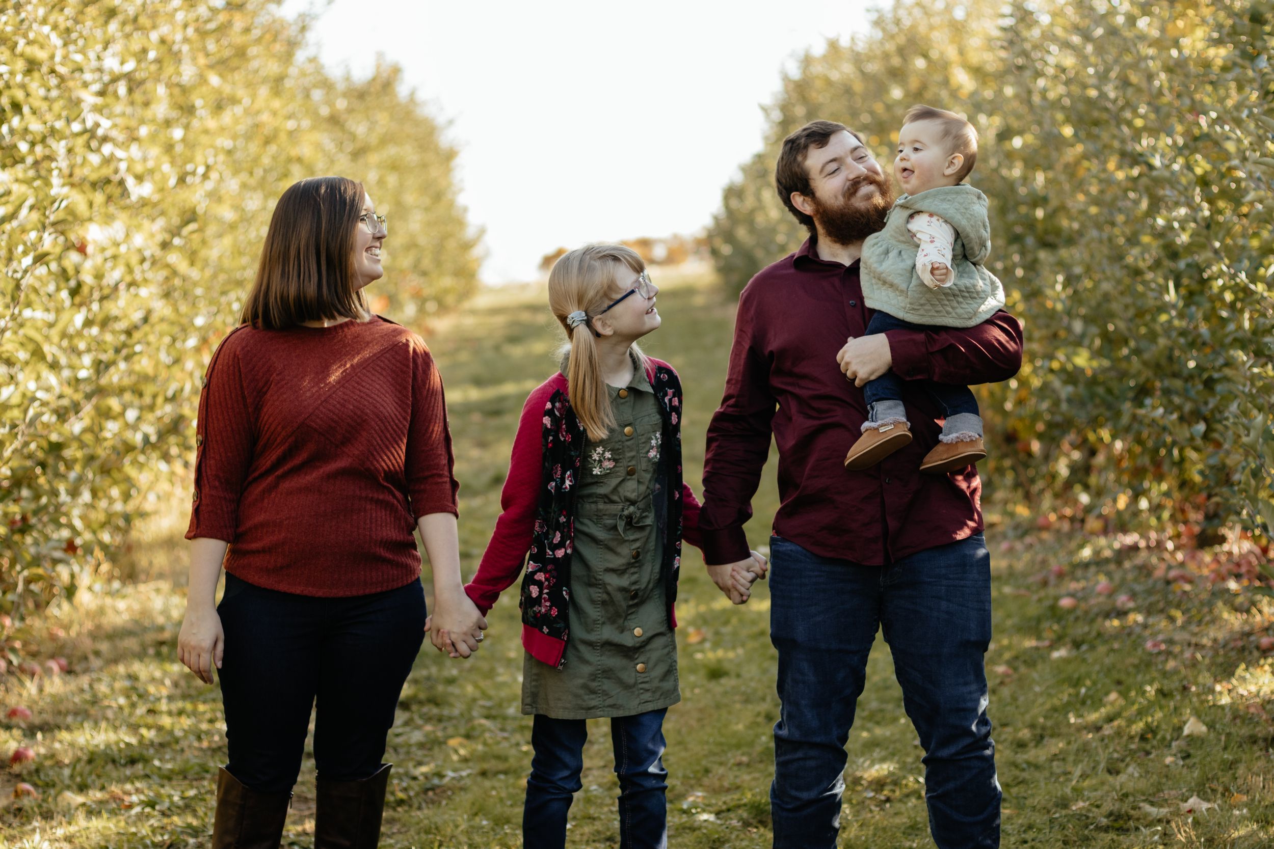Candid family moment captured against autumn trees with warm burgundy and olive outfits.