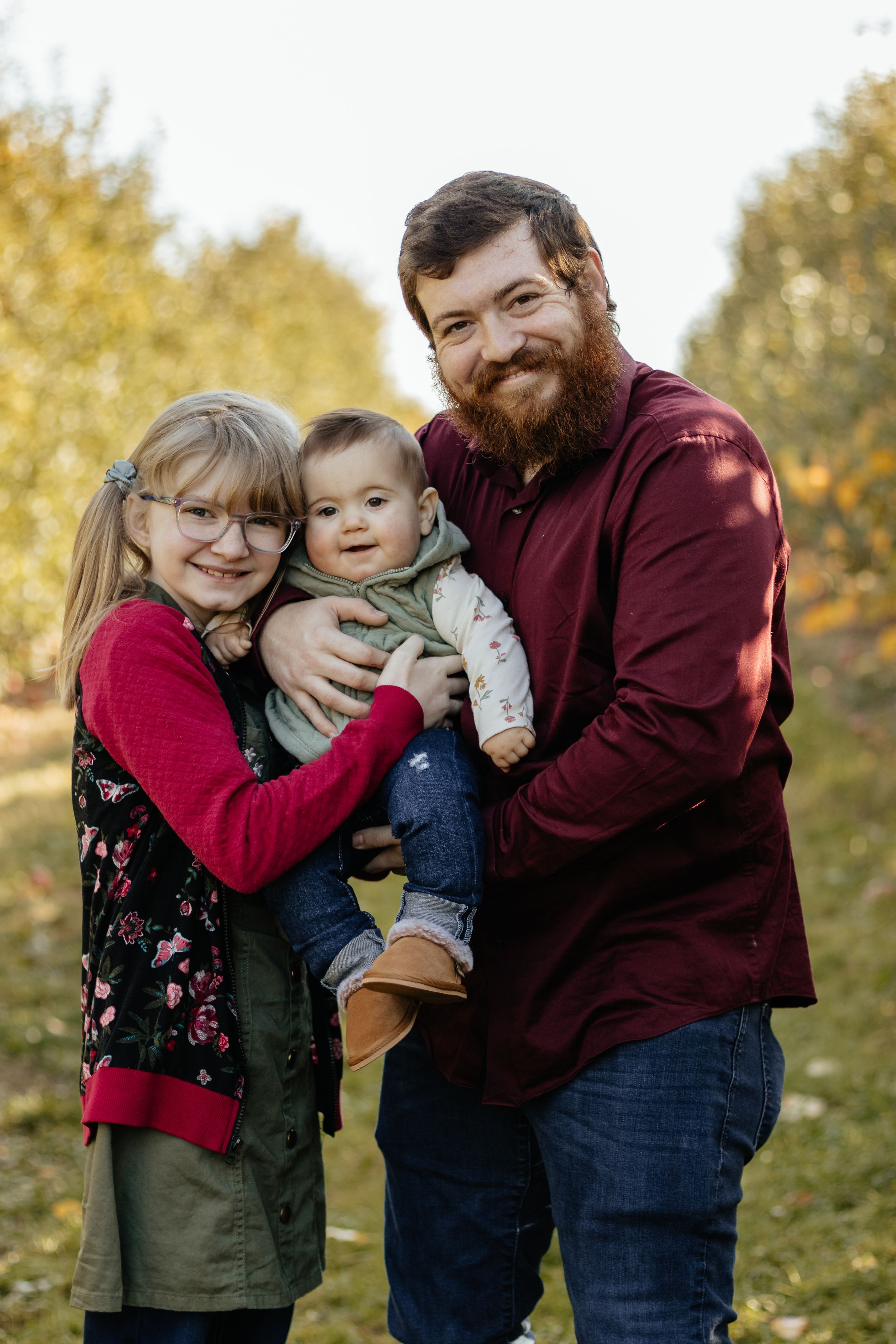 Family embracing during autumn photoshoot with warm burgundy and olive colored clothing.