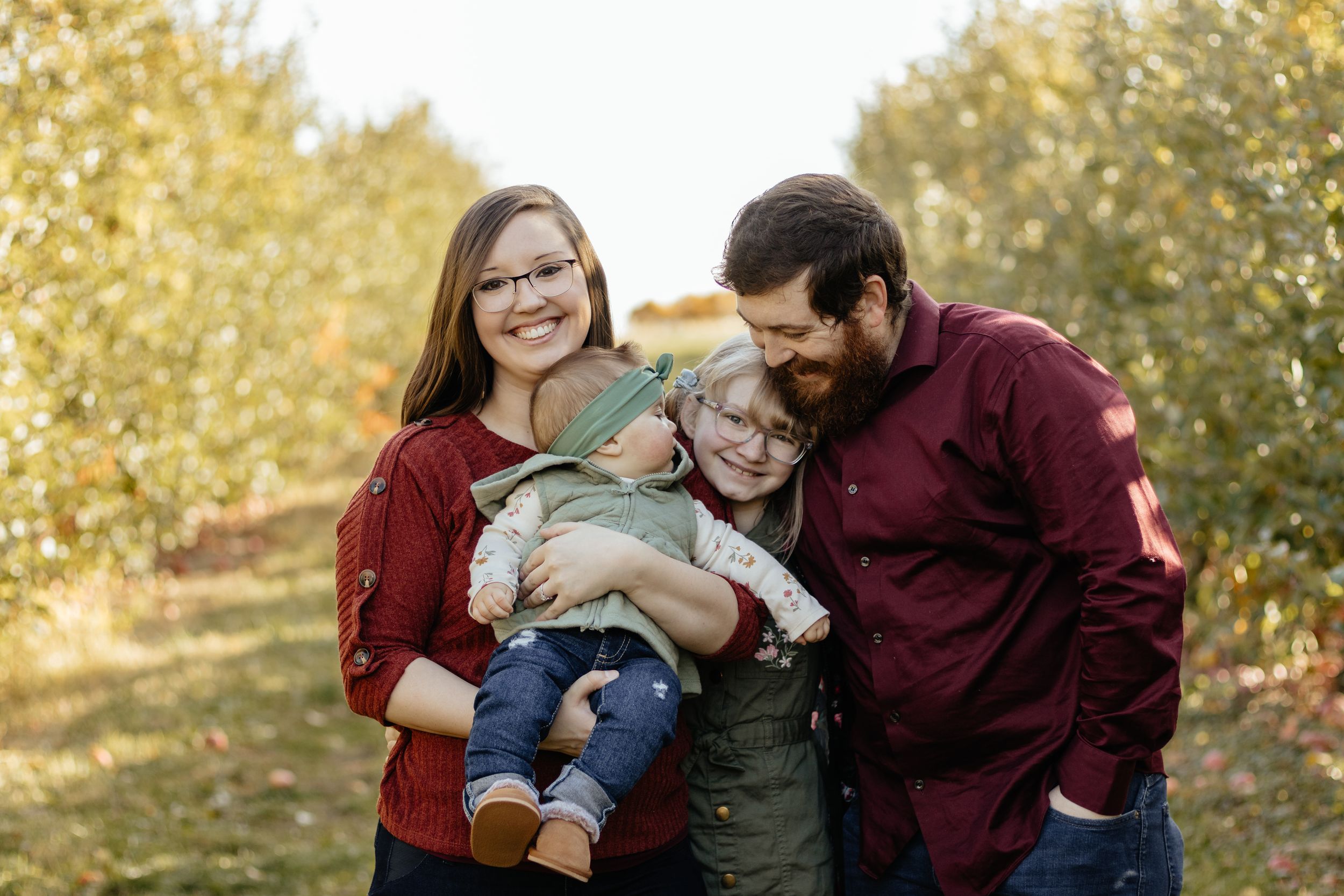 Natural family portrait session with golden autumn trees and warm-toned outfits.